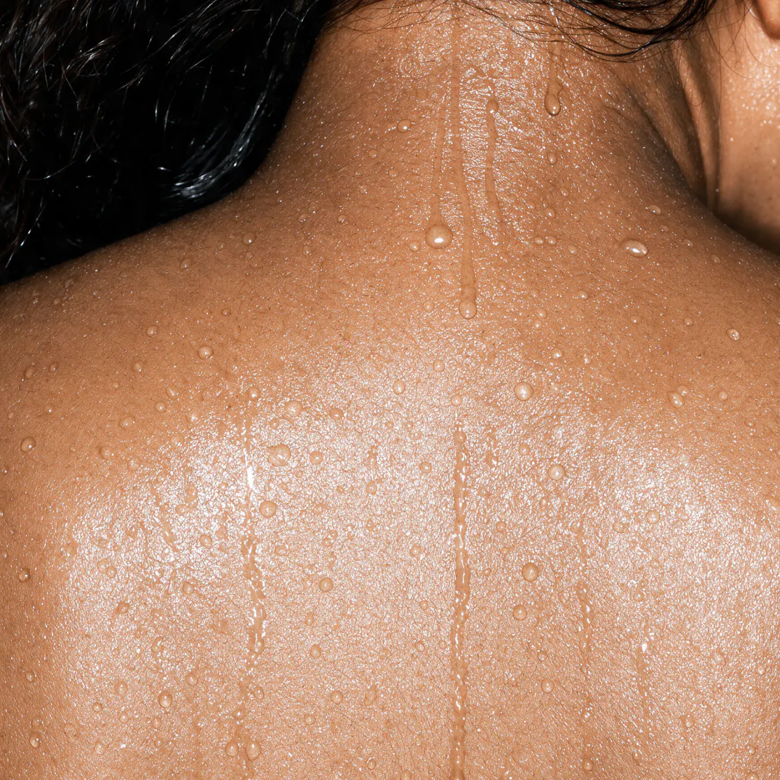 A close-up photo of a woman's back glistening with sweat. She's experiencing a hallmark menopause symptom: a hot flash.