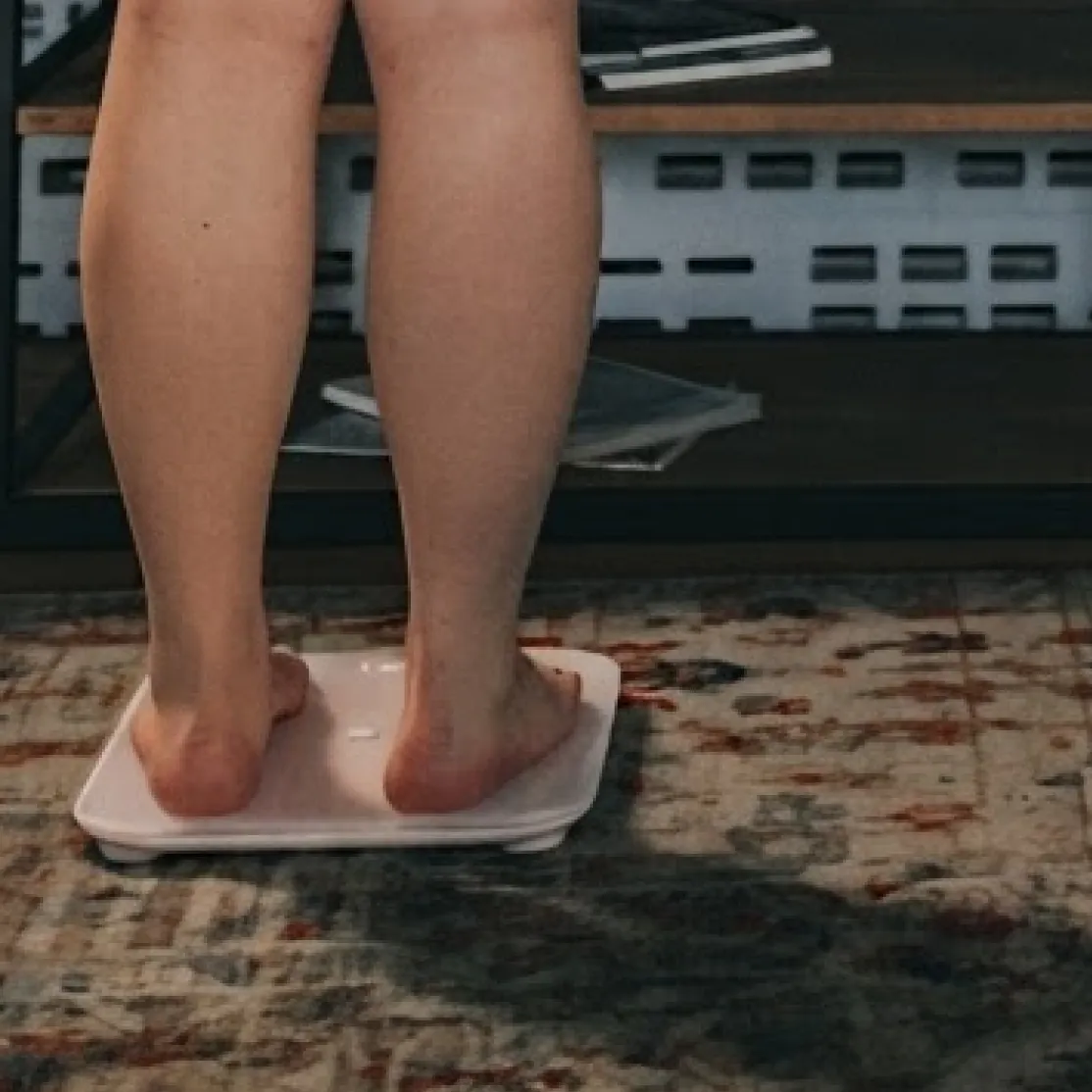 A close-up photo of a woman in midlife stepping on a scale at home.