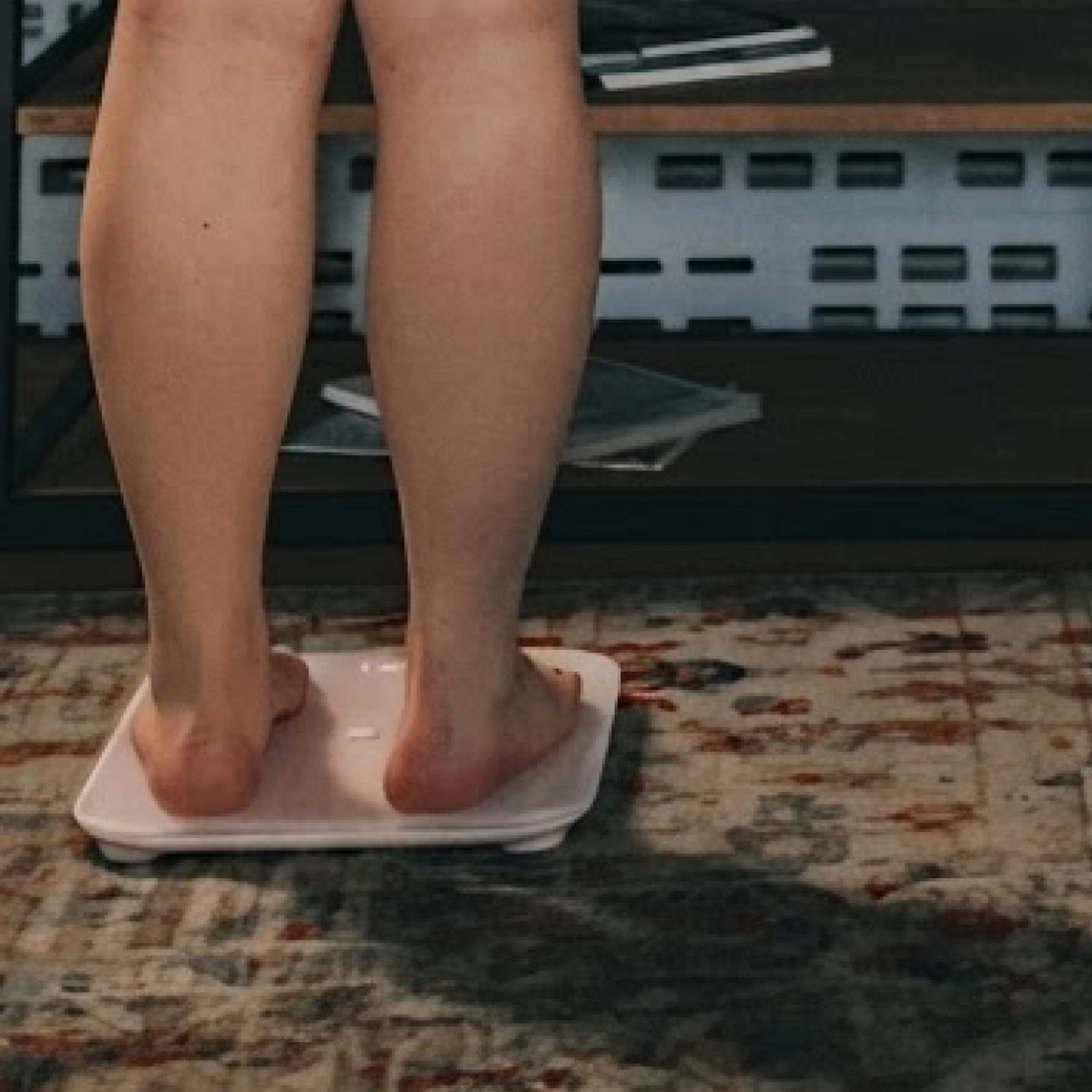 A close-up photo of a woman in midlife stepping on a scale at home.