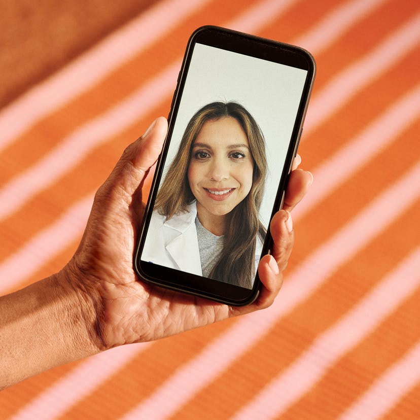 Photograph of hand holding phone with Midi clinician on telehealth