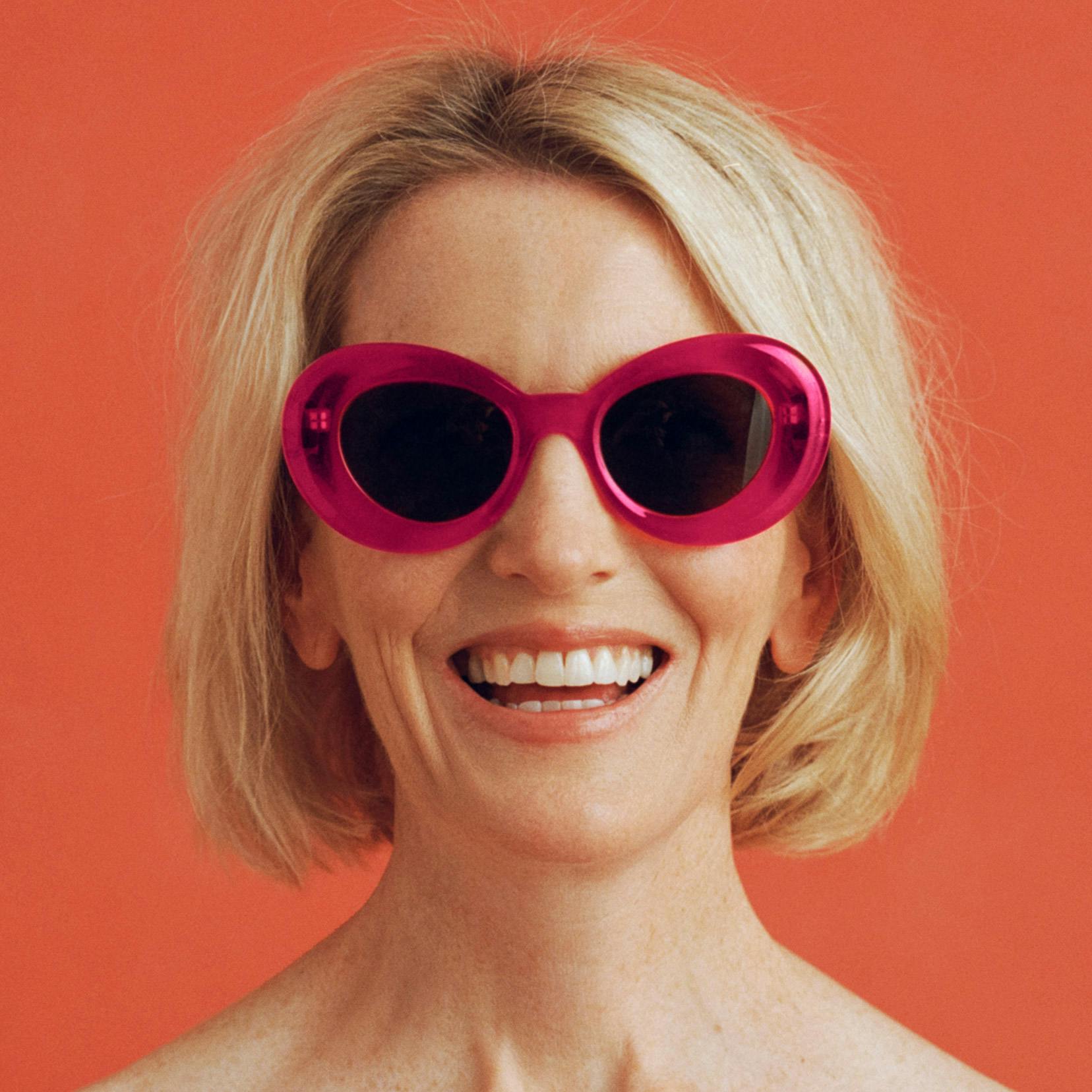 Photograph of woman wearing bright pink sunglasses and smiling