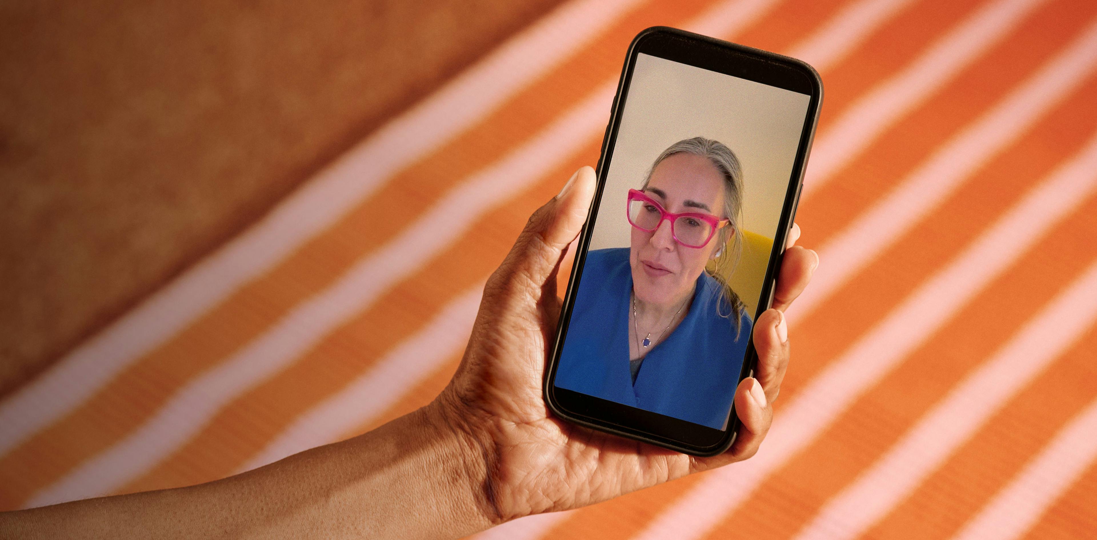 Close cropped photograph of woman's hand holding a phone with Midi clinician on telehealth