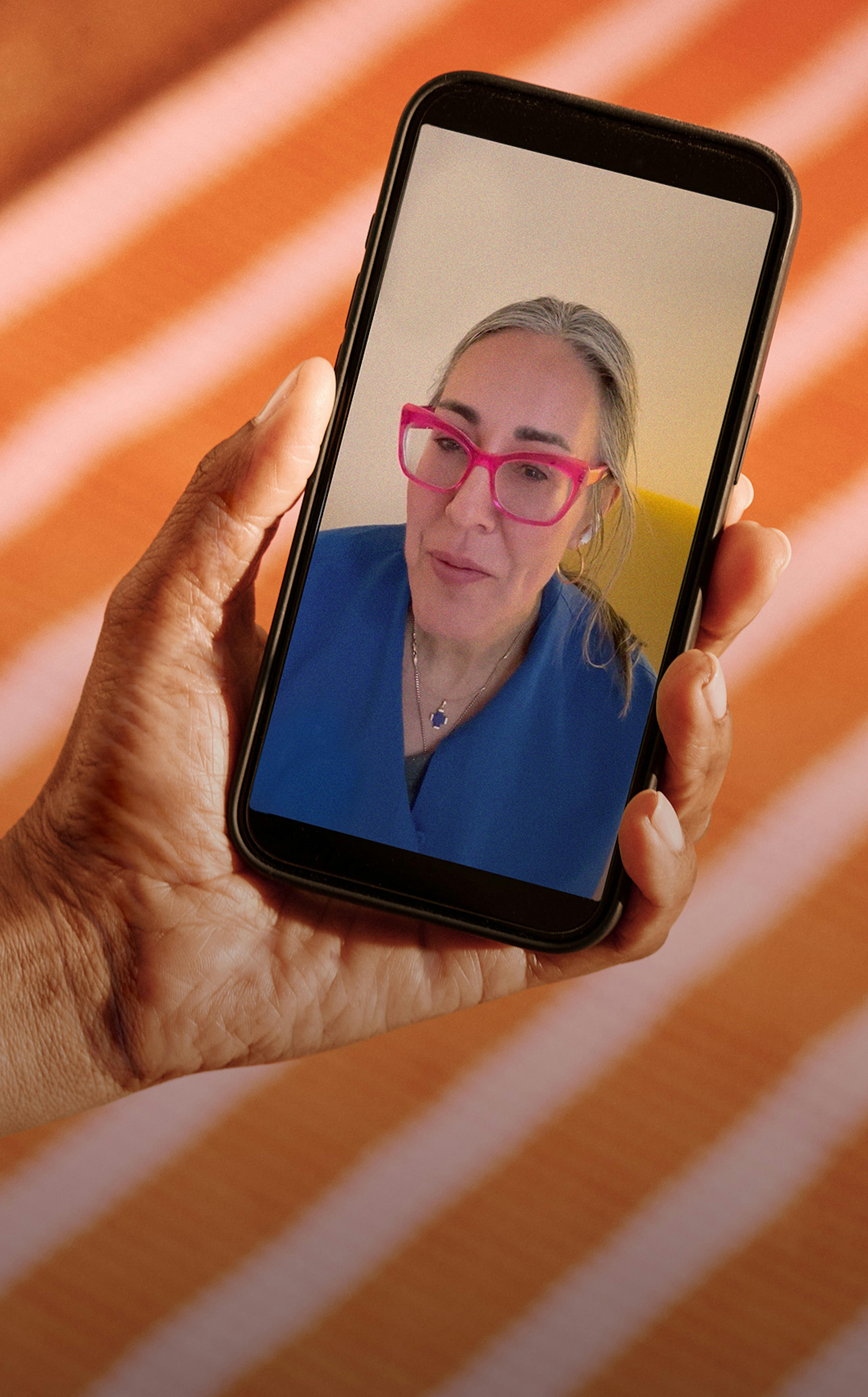 Close cropped photograph of woman's hand holding a phone with Midi clinician on telehealth