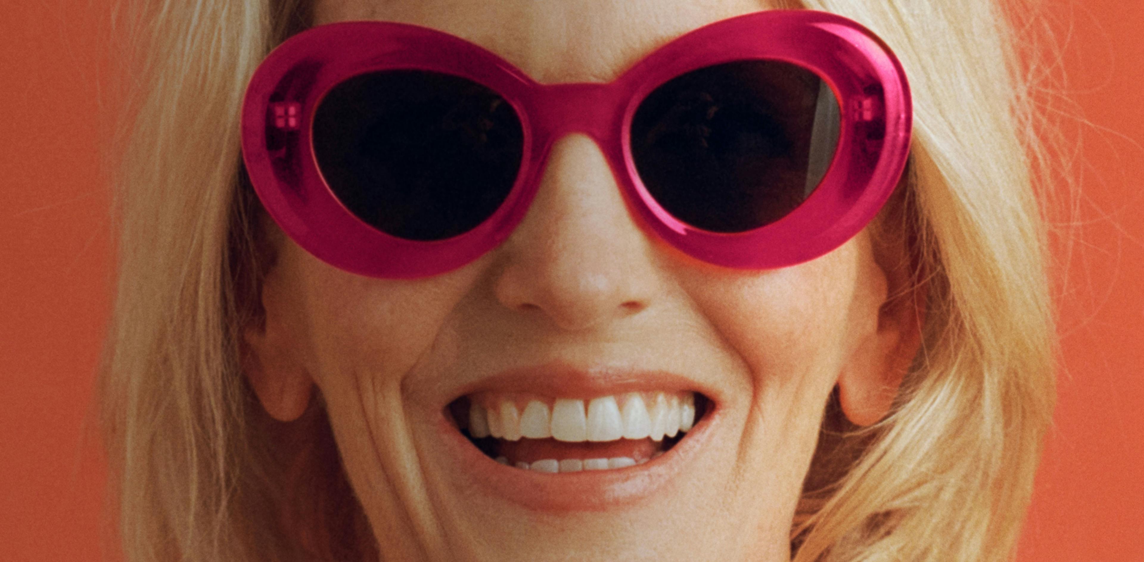 Portrait photograph of woman smiling while wearing hot pink sunglasses