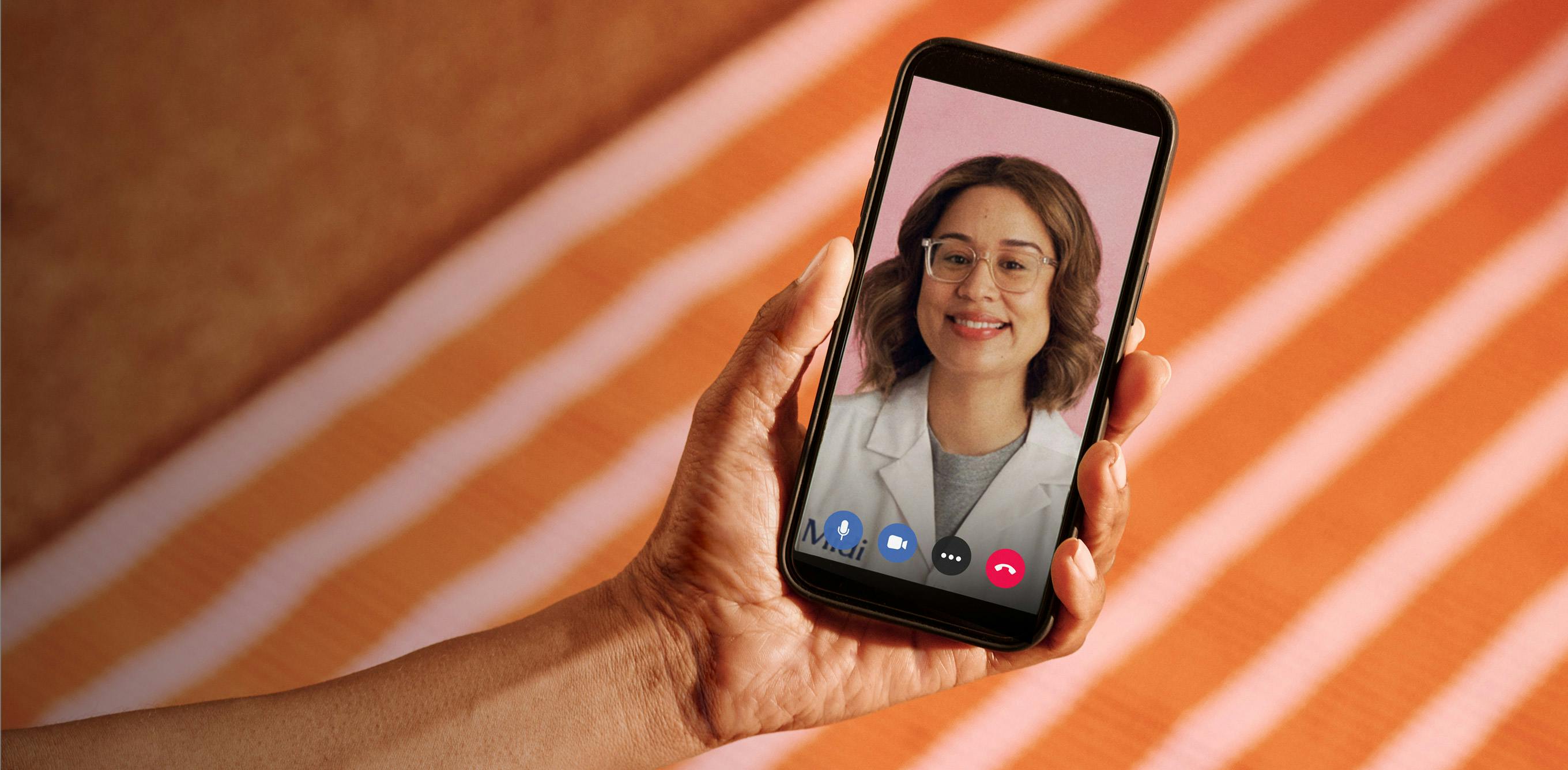 Close cropped photograph of woman's hand holding a phone with Midi clinician on telehealth