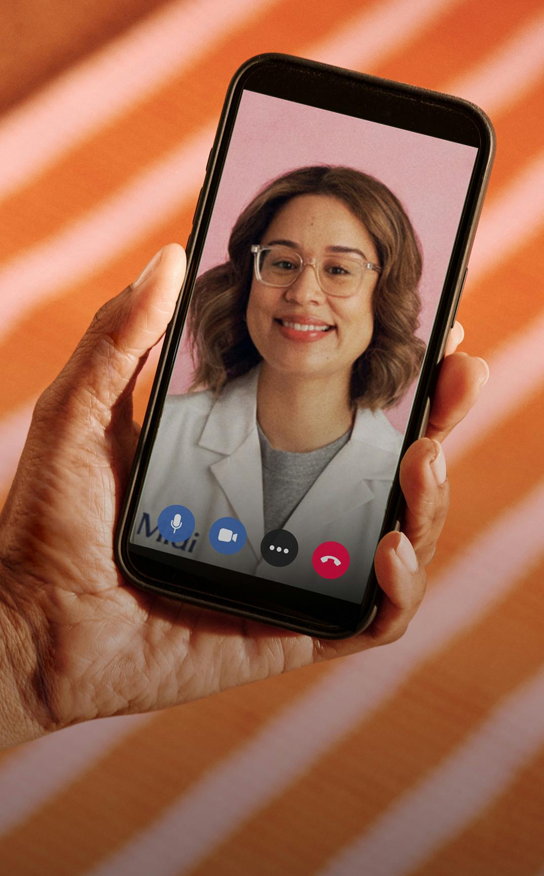 Close cropped photograph of woman's hand holding a phone with Midi clinician on telehealth