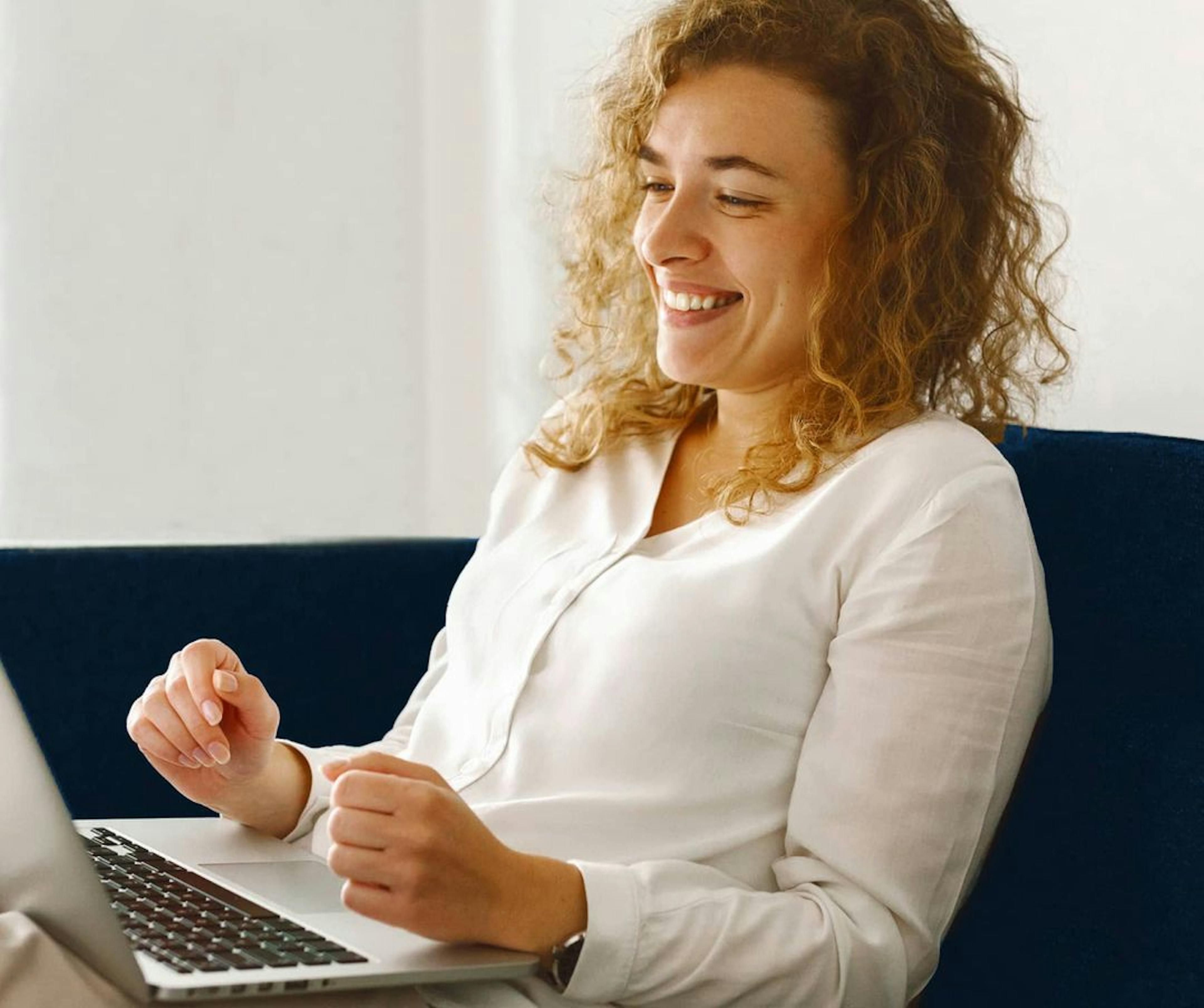 woman sitting down and smiling at laptop screen