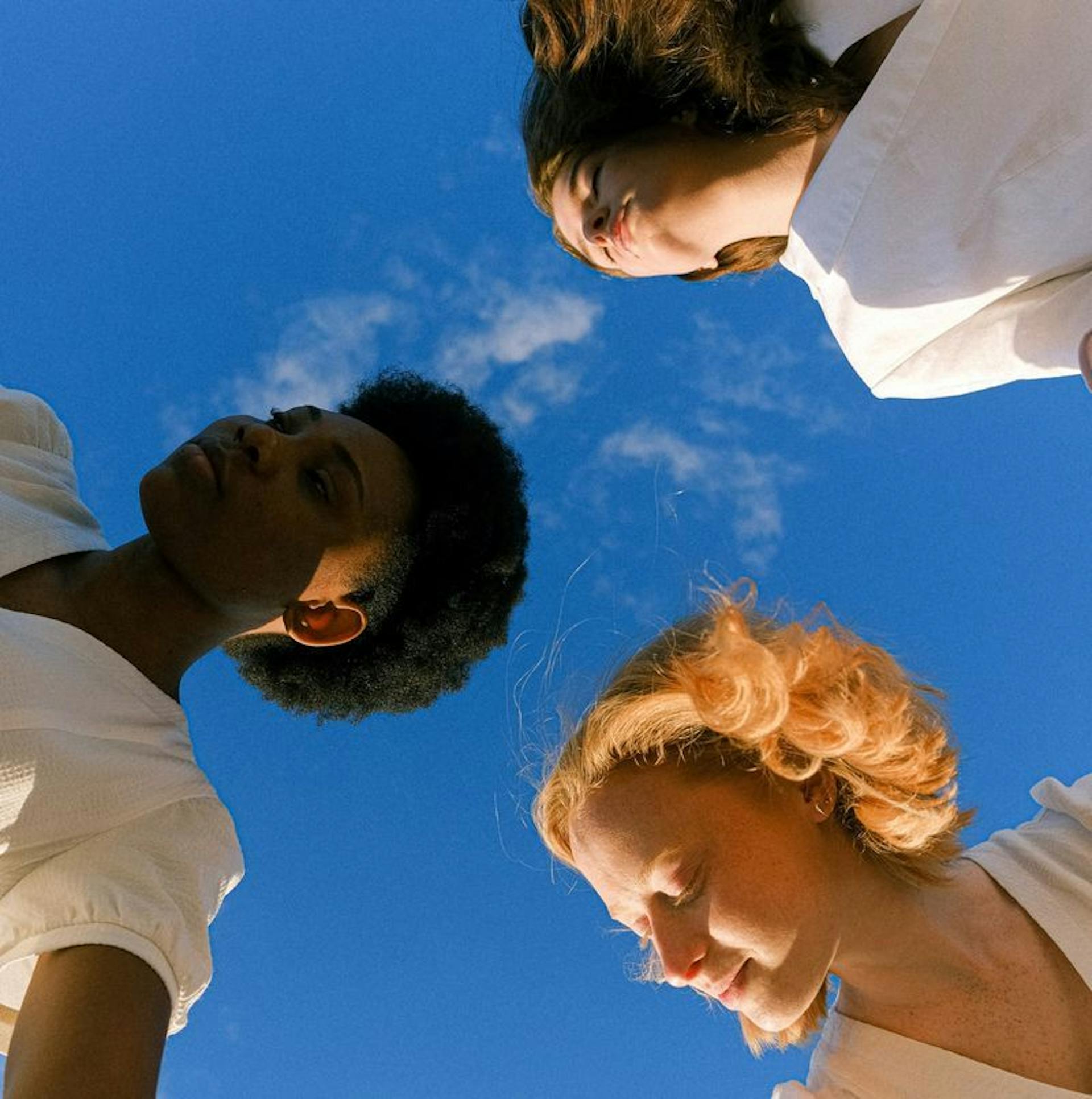 3 women with eyes closed and blue sky above them