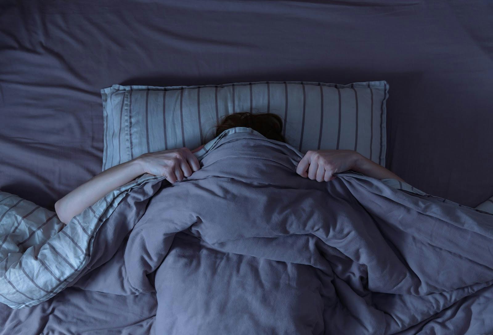 Woman In a rumpled bed pulling the covers over her face