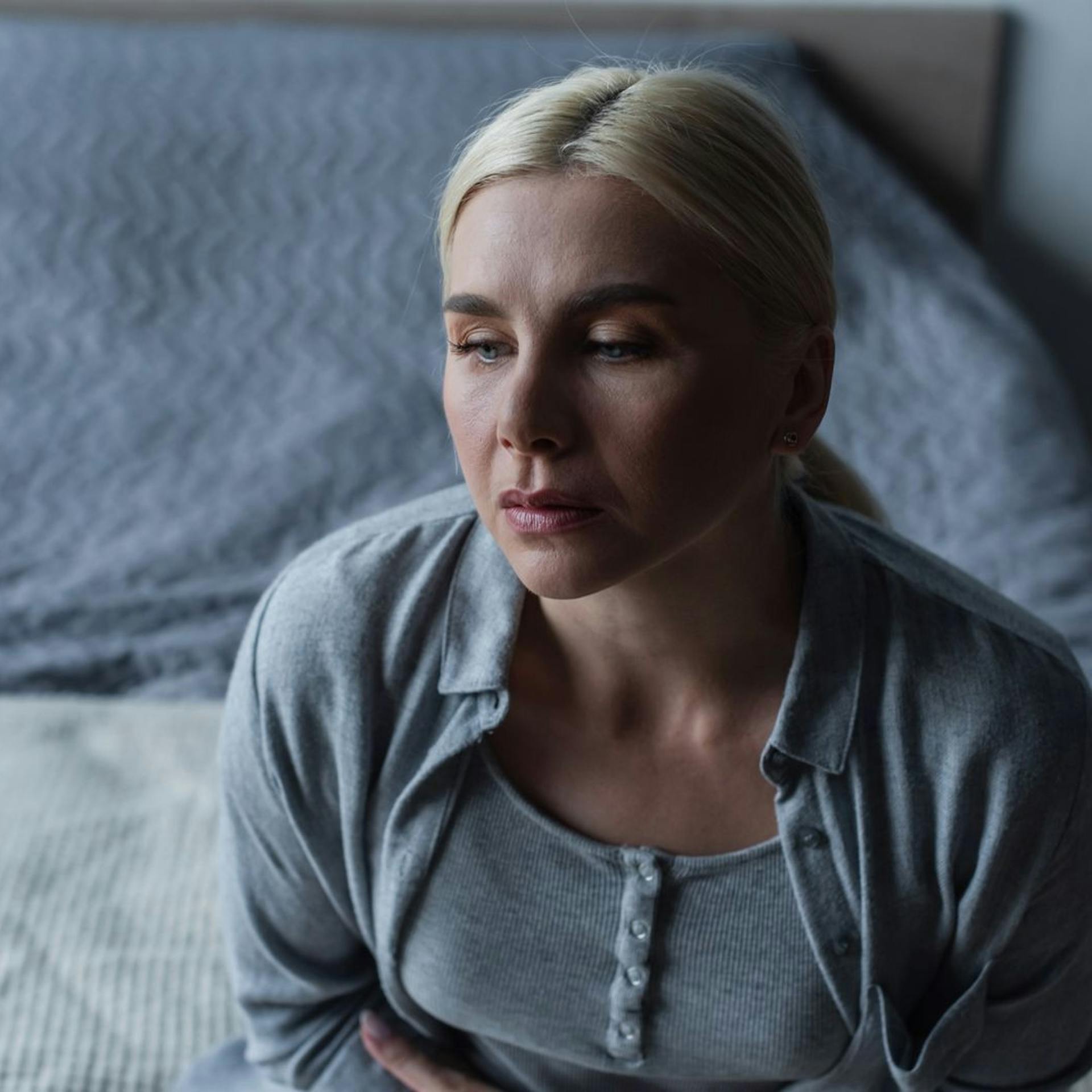 Woman sitting on the edge of a bed, holding her stomach