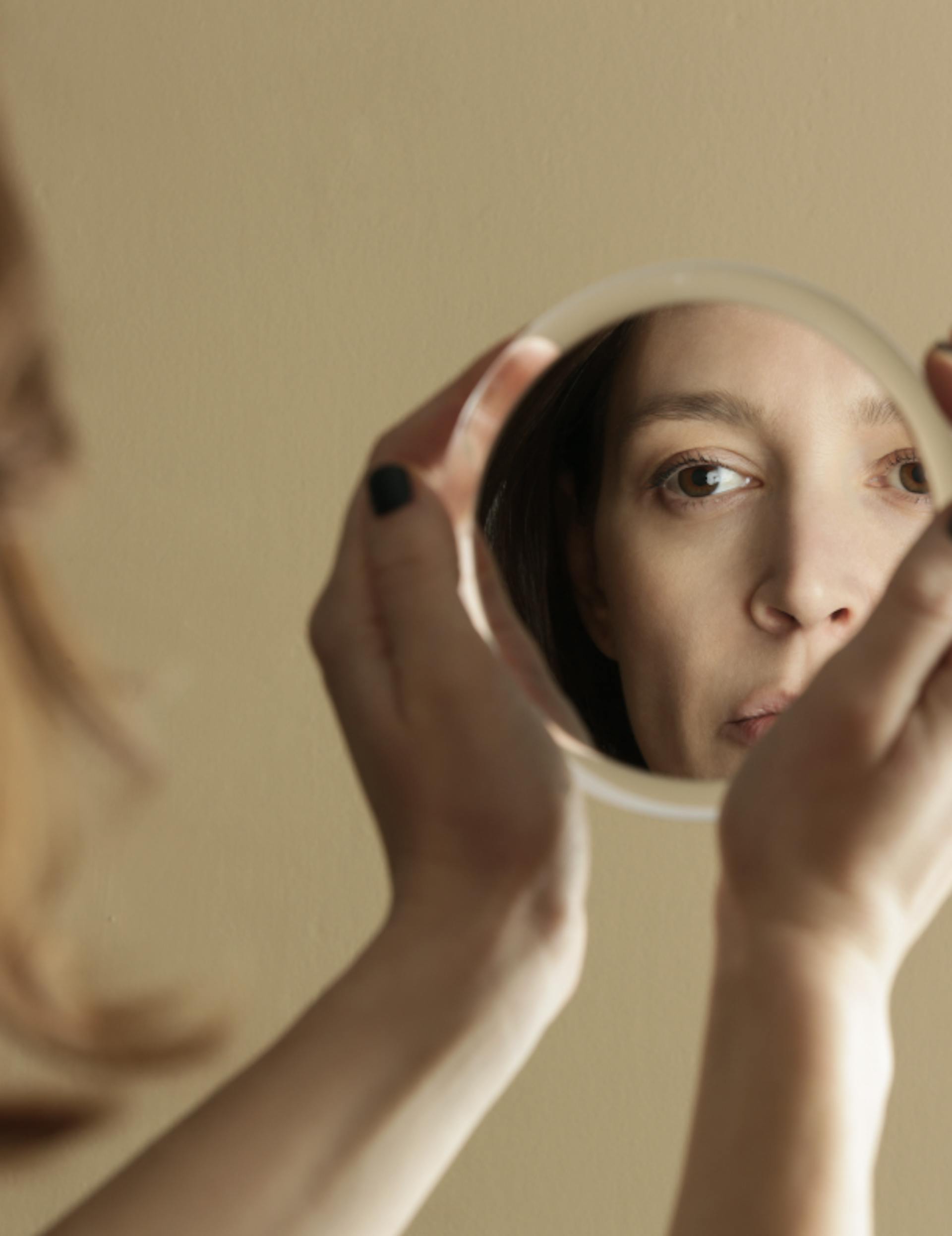 woman looking In a small round mirror at her hair and skin