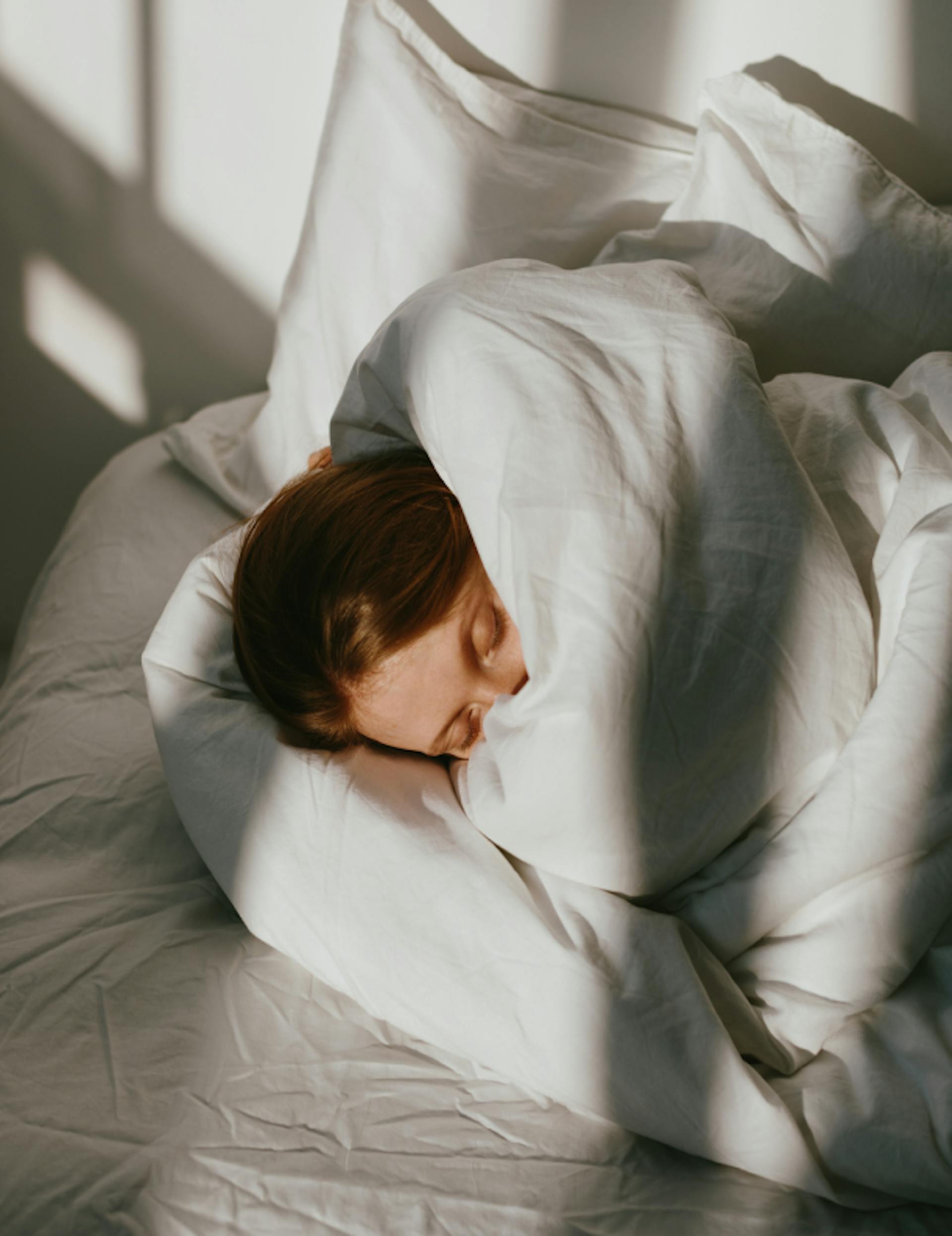 Woman holding her hands over her face while lying In bed