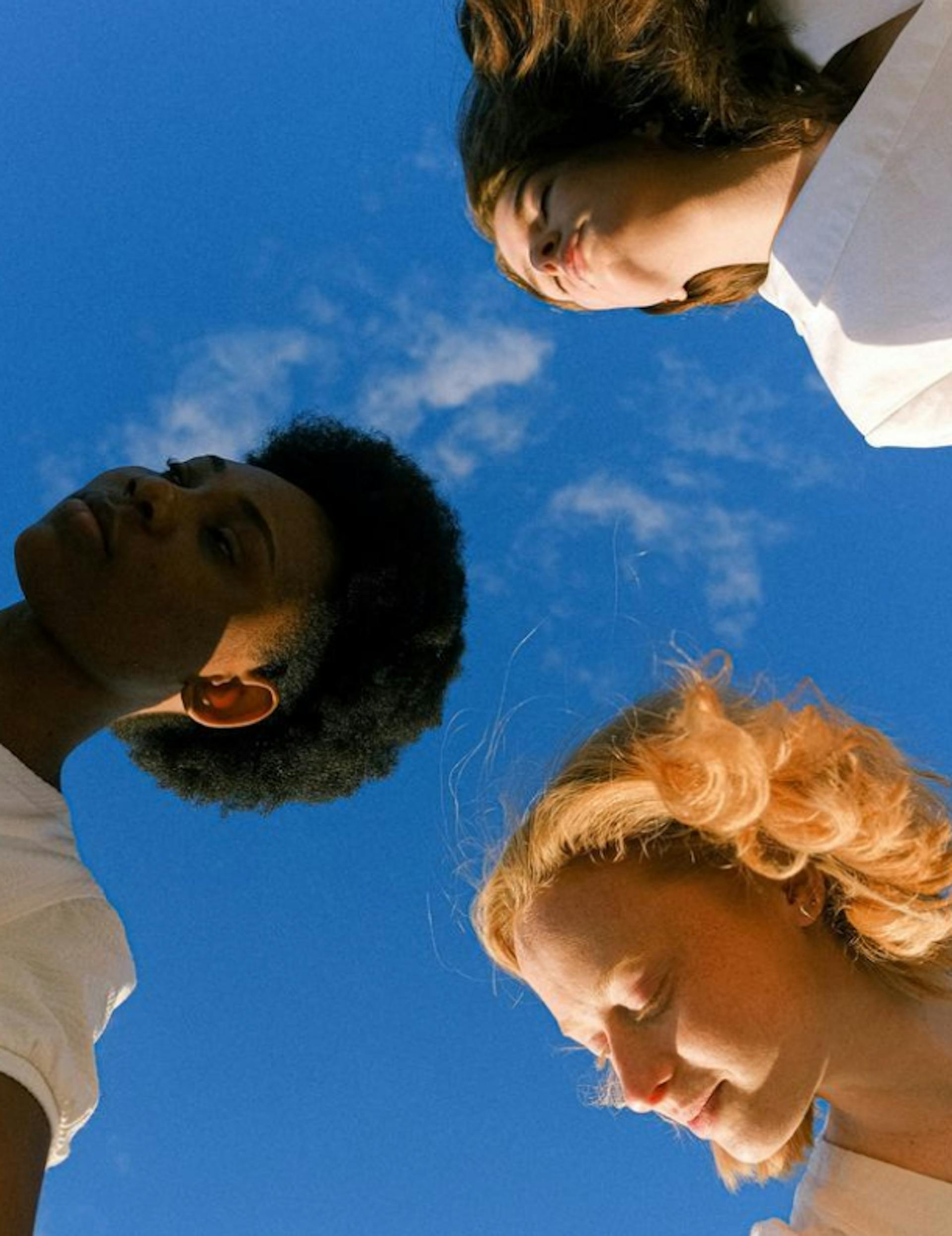 3 women with eyes closed and blue sky above them