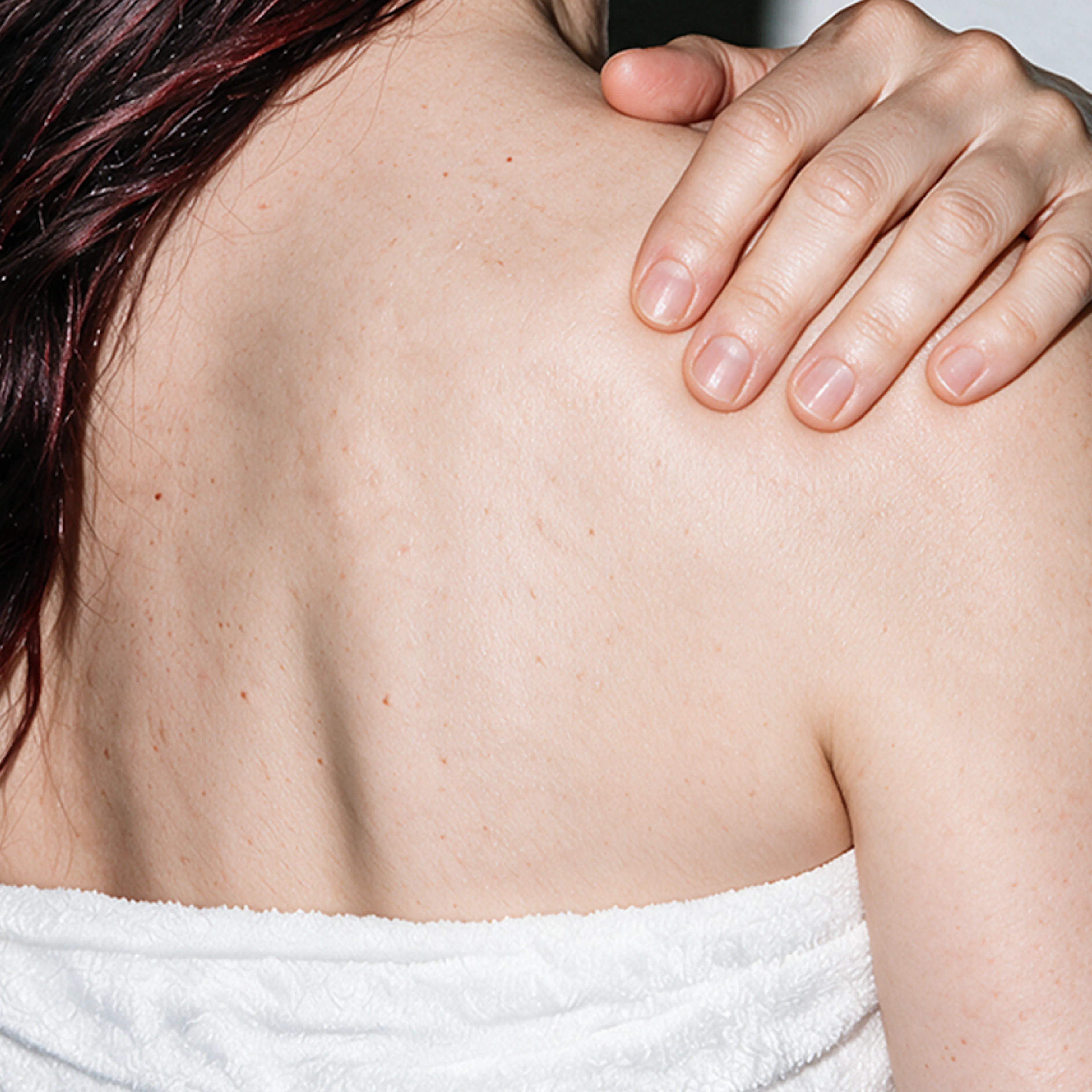 A close-up view of a woman holding onto her back. She is dealing with itchy skin, a weird perimenopause symptom.