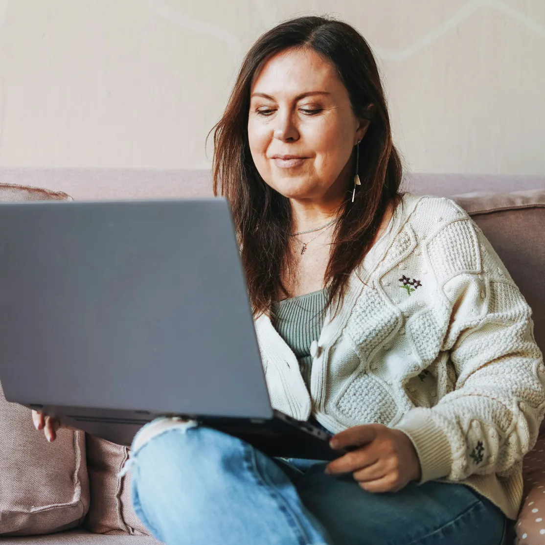 A woman in midlife looking at her laptop while sitting down on a couch.