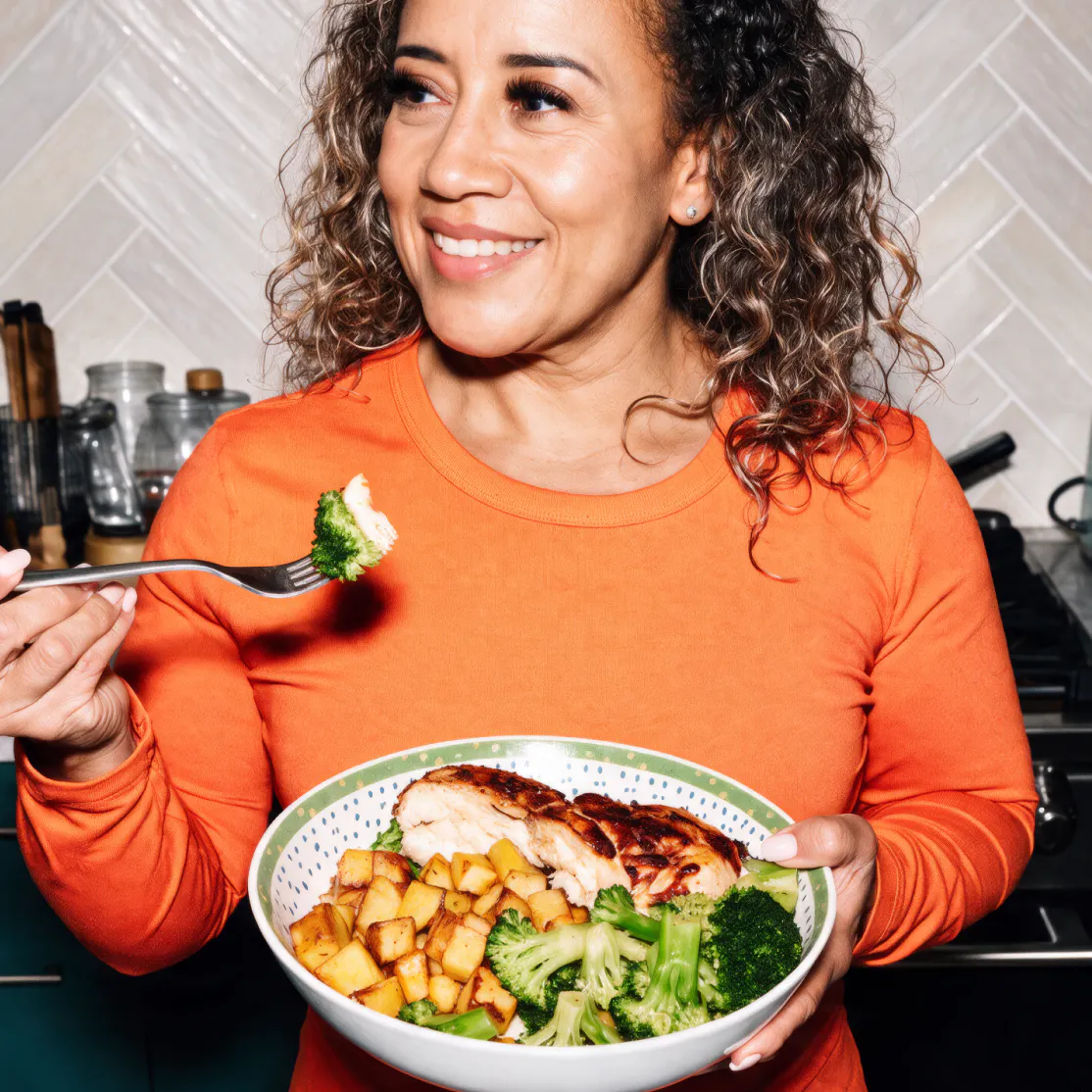 A woman in menopause eating a protein-forward meal with chicken and broccoli.