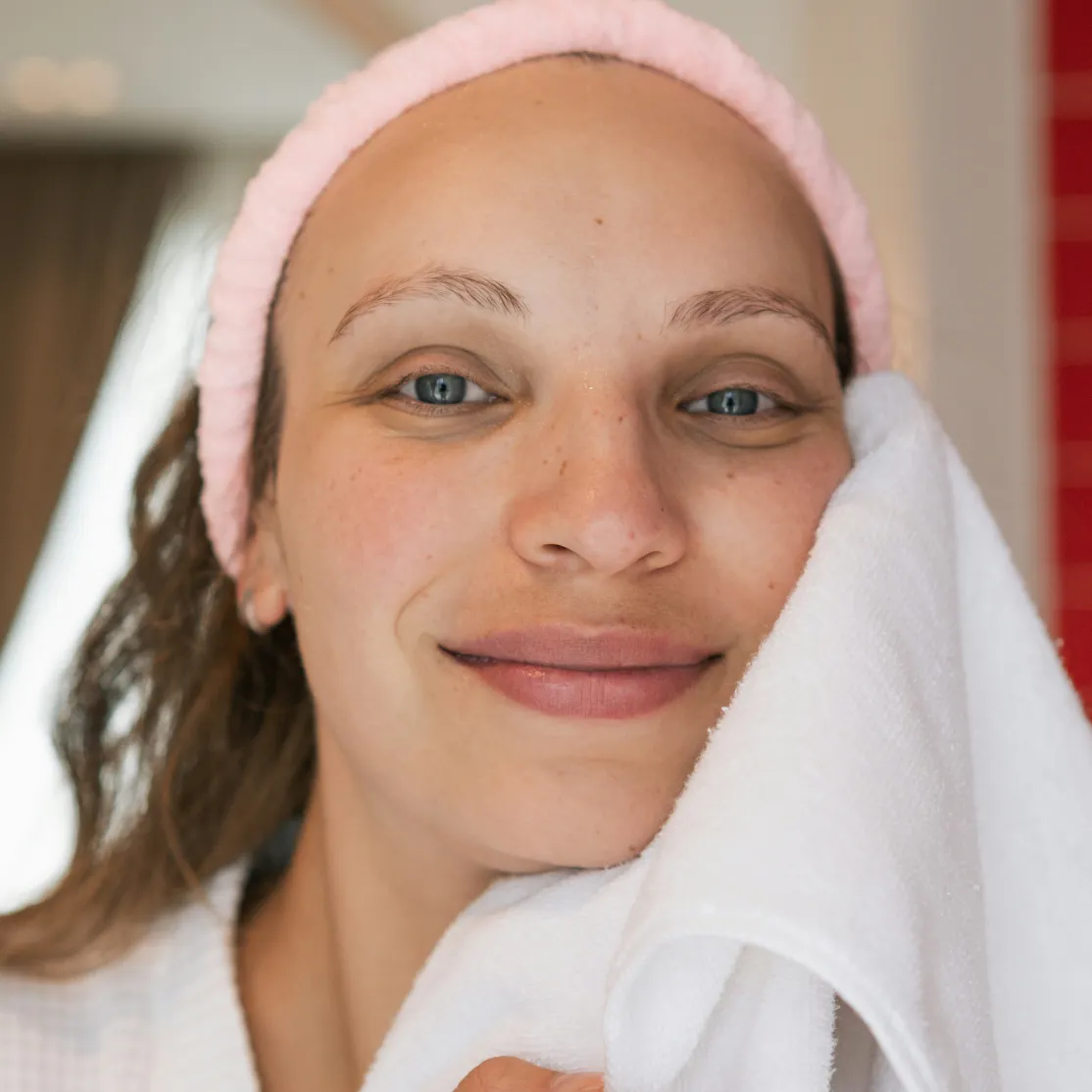 A woman in midlife smiling and wiping her face with a towel, looking into the camera.