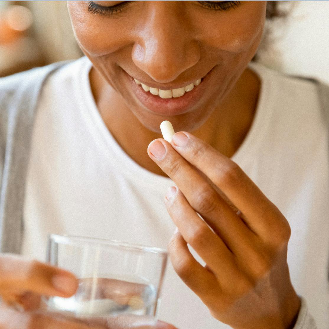 picture of a woman holding a glass of water, about to take a pill