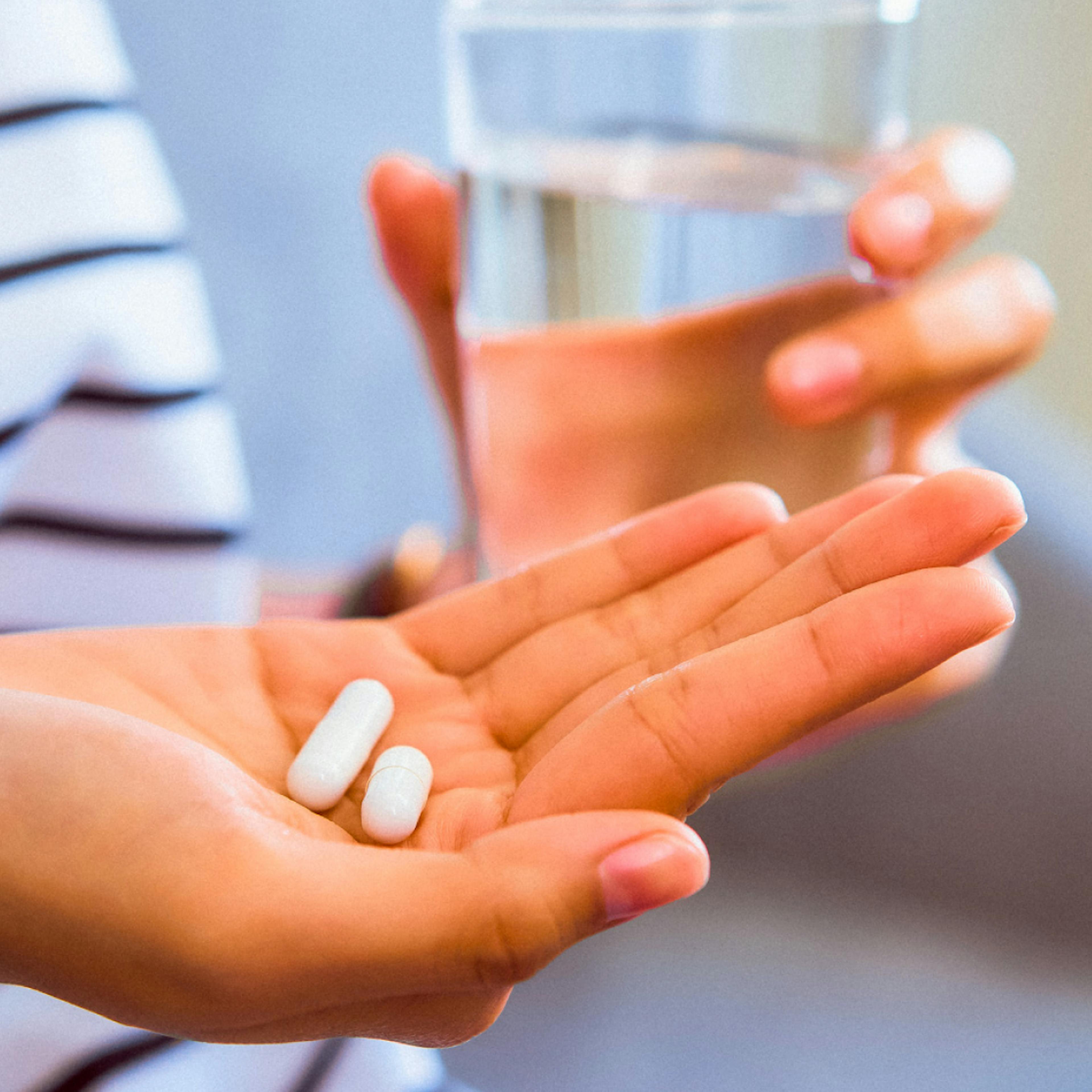 Woman holding low dose naltrexone pills with cup of water