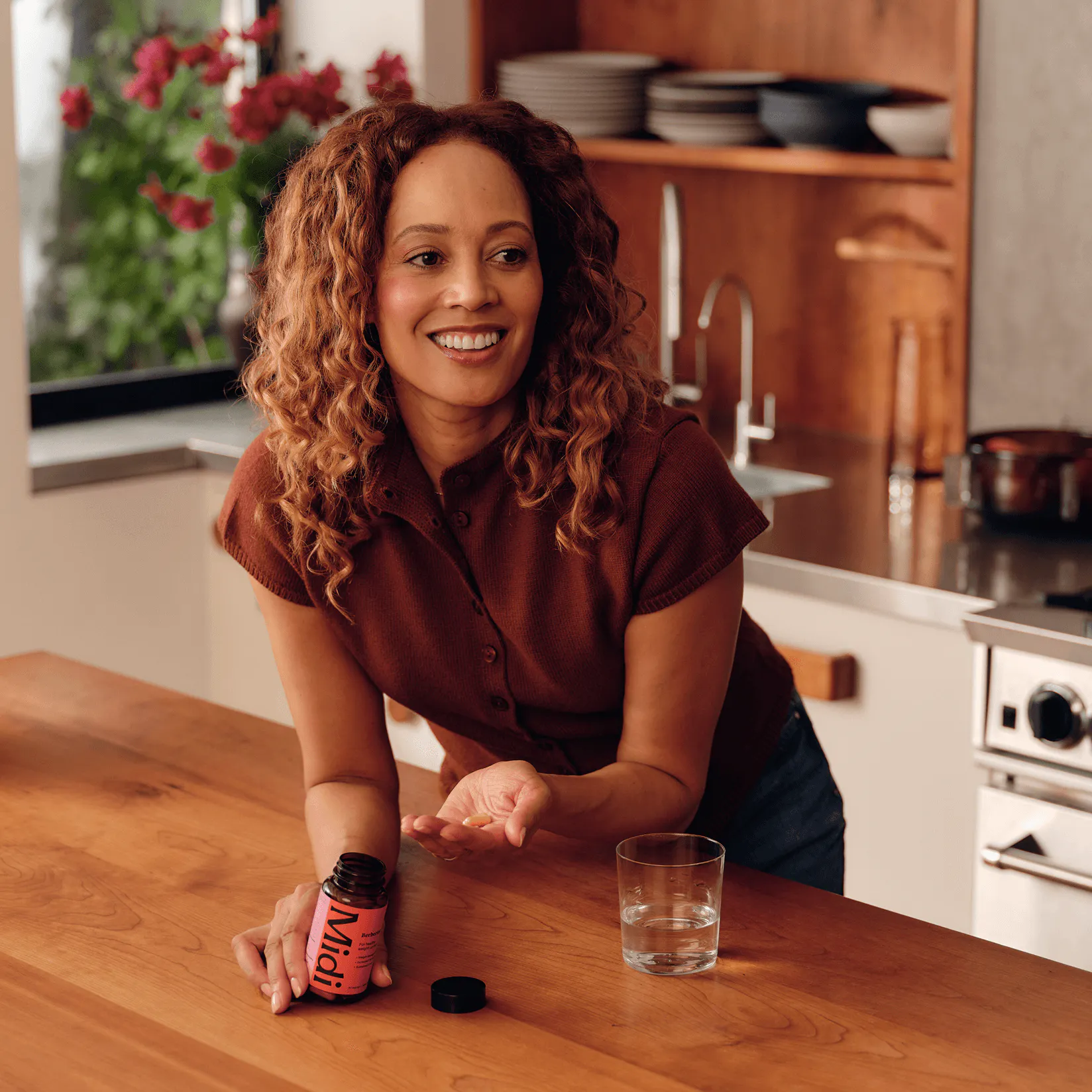 A woman at her kitchen Island smiling while holding a Midi supplement