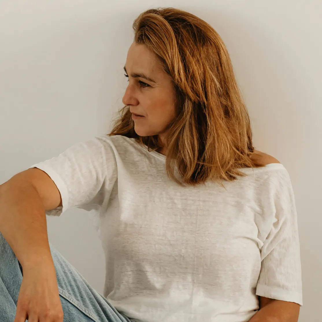A woman thinking about her FSH levels. She's wearing a white tee and looking to the side.