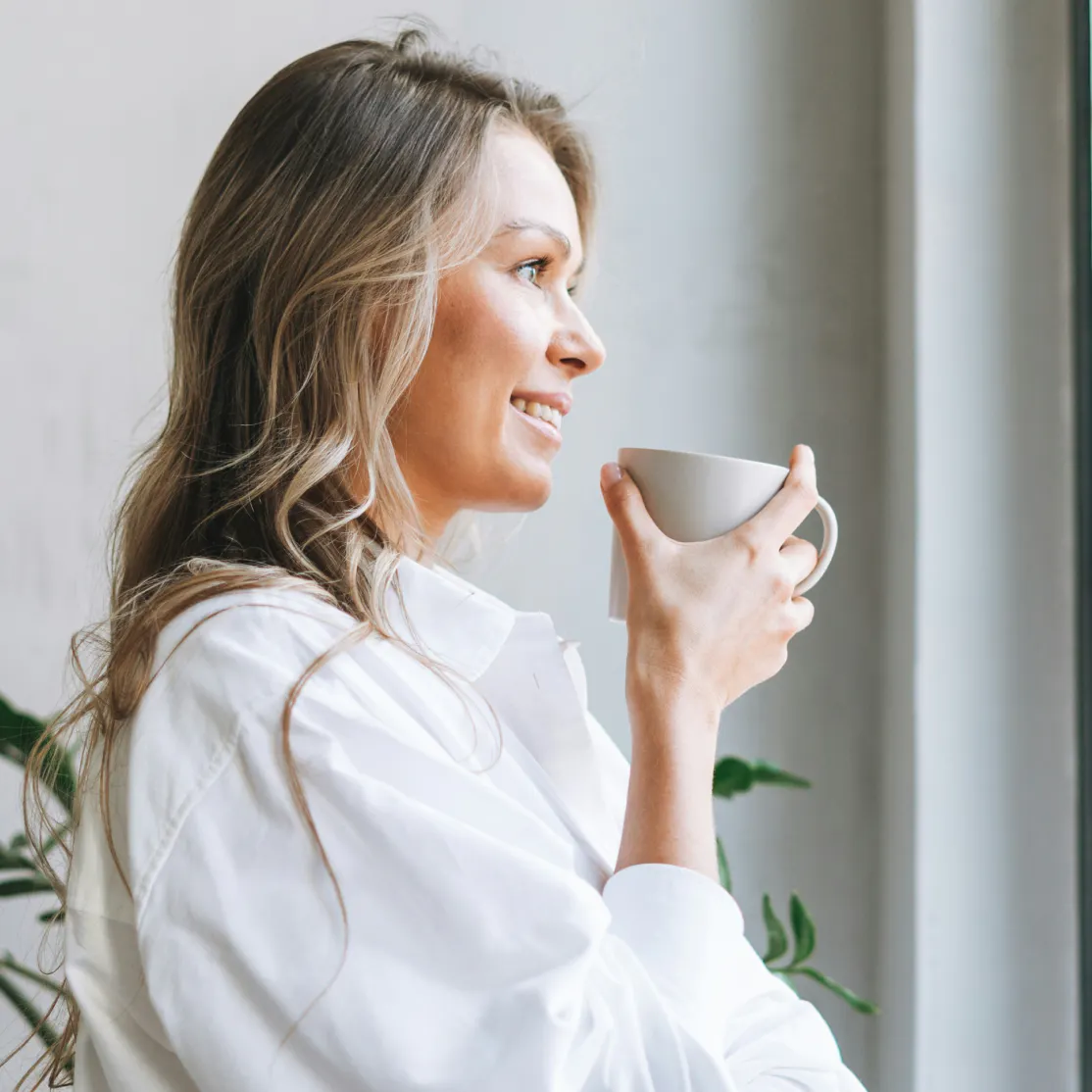 A woman in midlife sipping from a mug while she considers metformin for longevity.