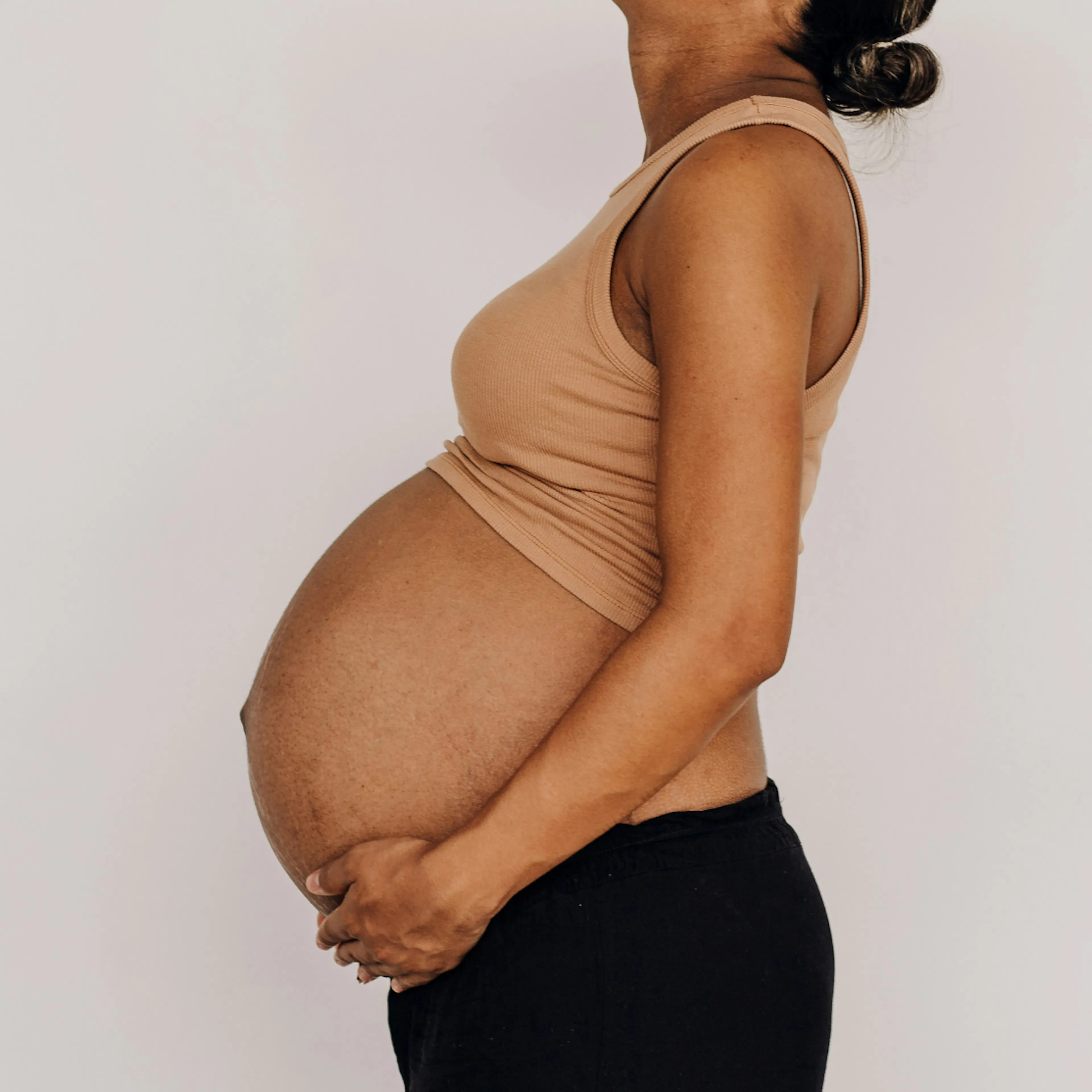 A close-up photo of a woman cradling her pregnant belly as she looks up. She is pregnant during perimenopause.