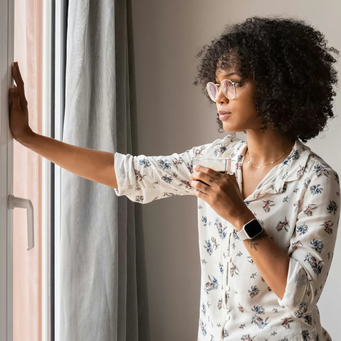 A woman in midlife drinking coffee with her hand on the wall. She is debating taking a perimenopause test.