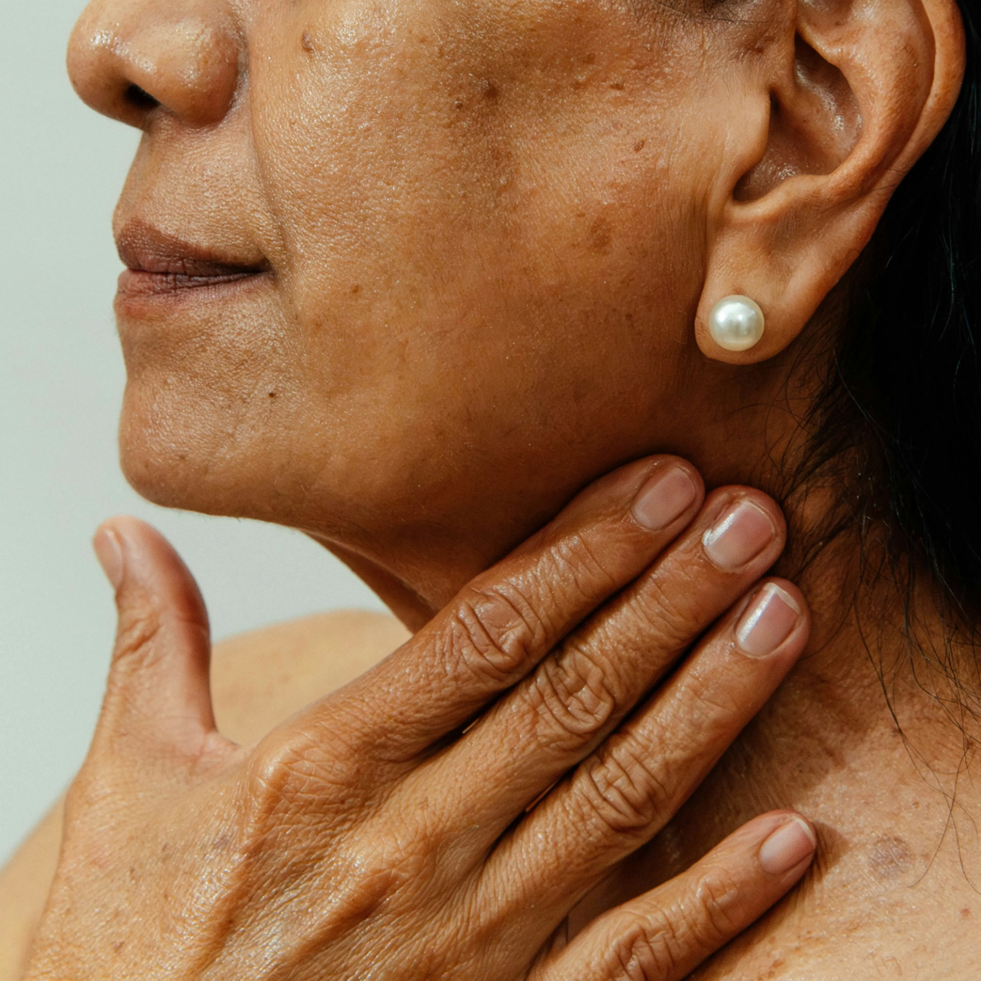 A close-up photo of a woman in midlife. She is touching her neck, rubbing in topical GHK-Cu.
