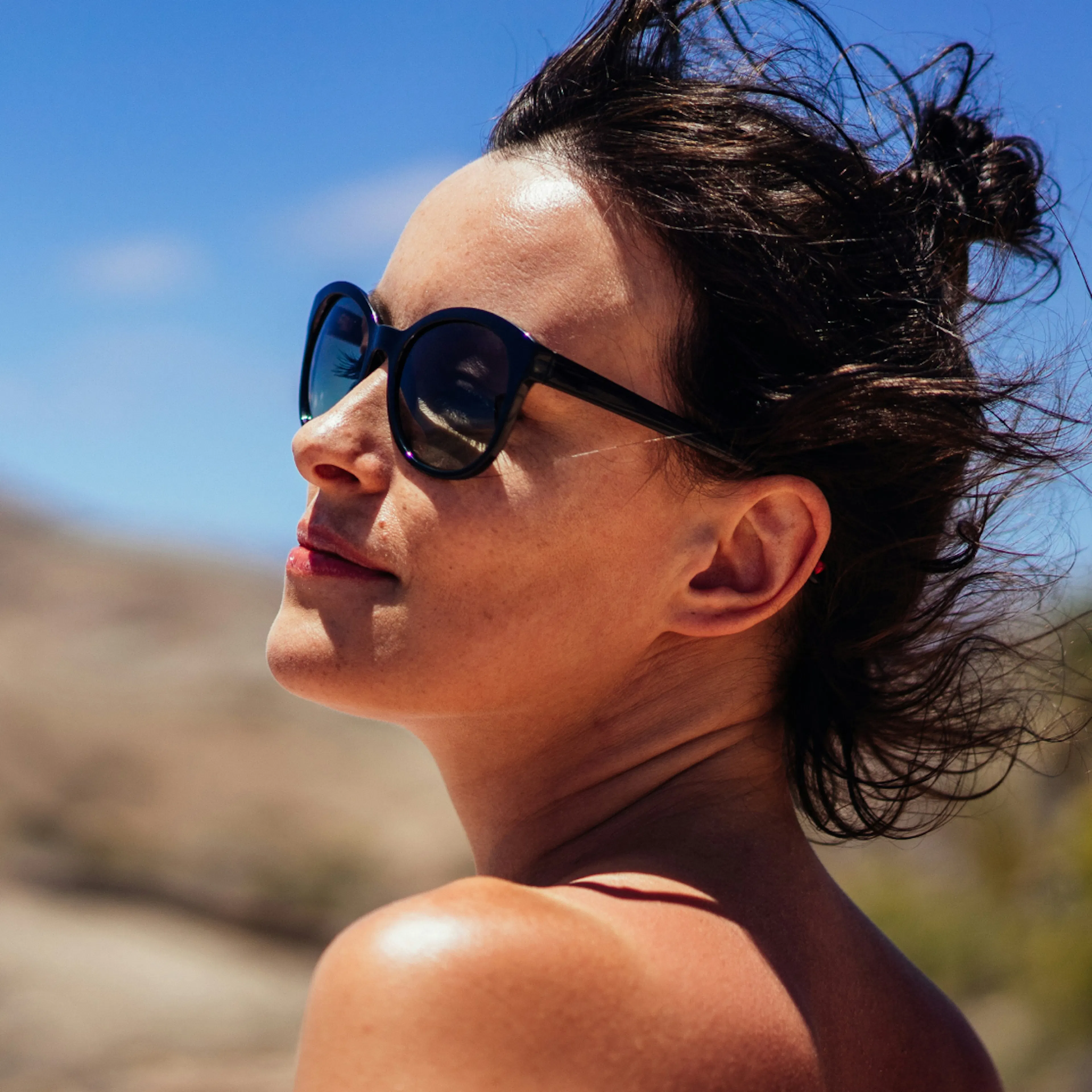 A woman in perimenopause outside looking to the side. She's wearing sunglasses and has short brown hair.