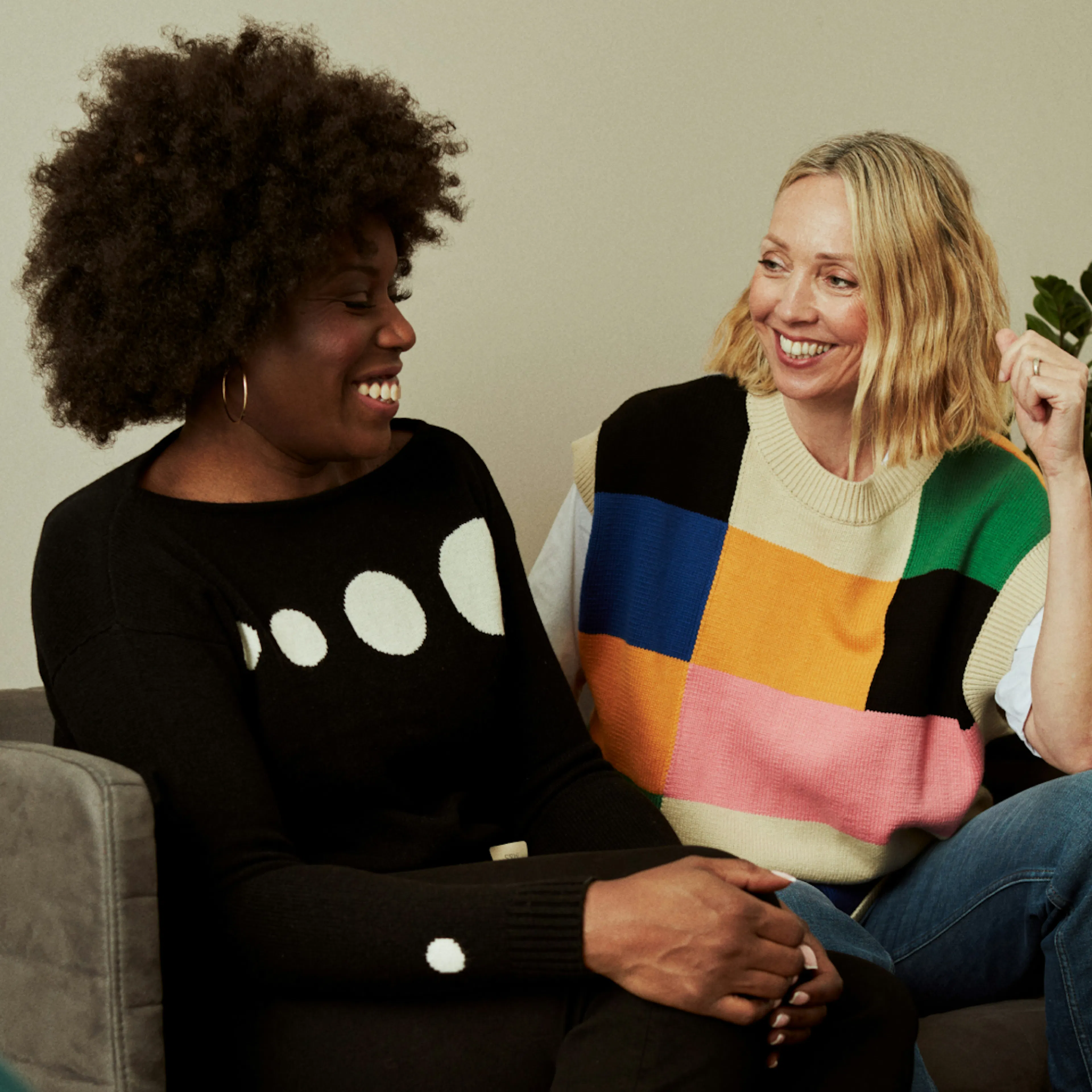 Two women in midlife smiling and sitting next to one another.