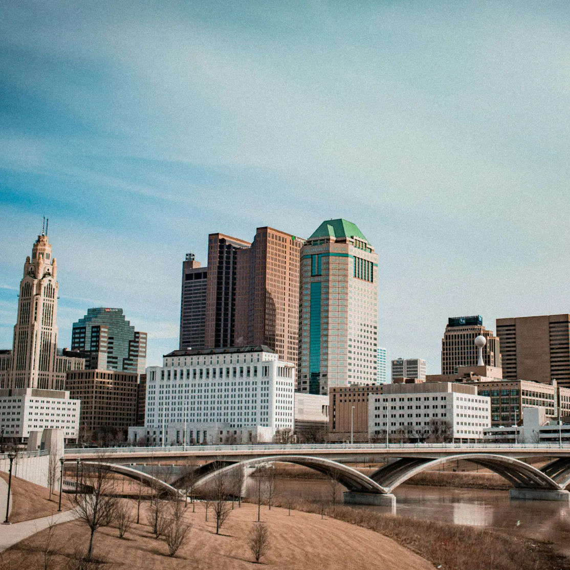 View of the downtown Columbus skyline with the Scioto River under a soft blue sky.