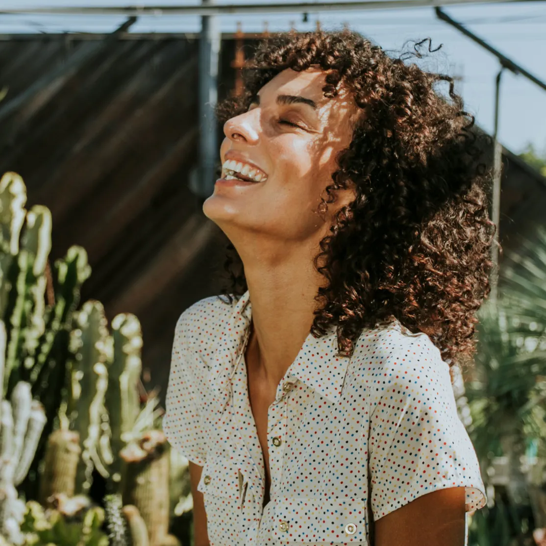 A woman in menopause smiling and laughing in front of cacti.