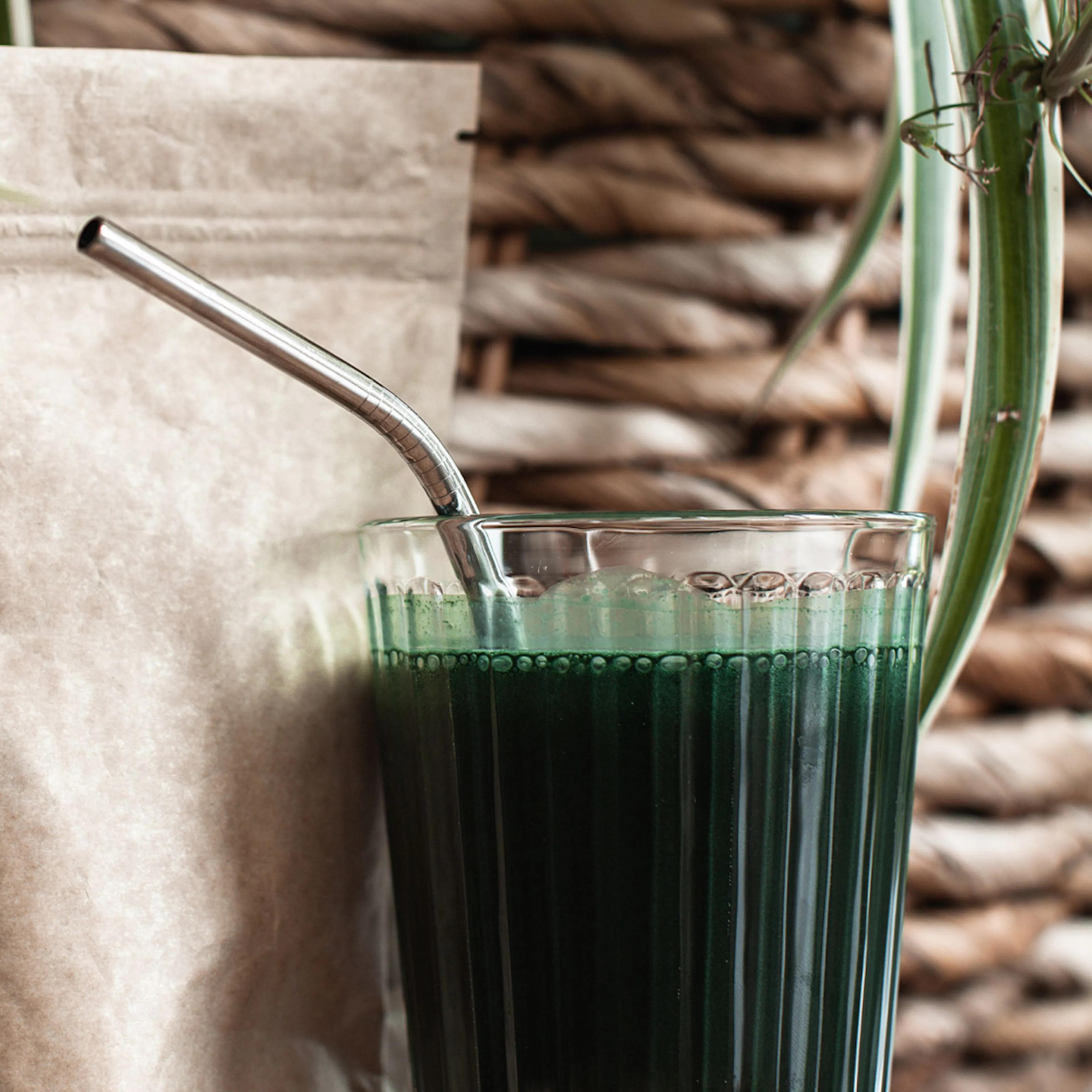 A green weight loss drink in a glass cup with a metal straw.