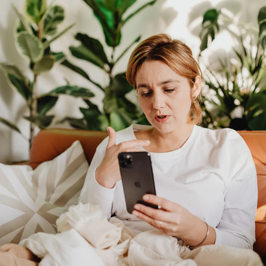 A woman in midlife, sitting at home and looking up progesterone side effects on her phone.