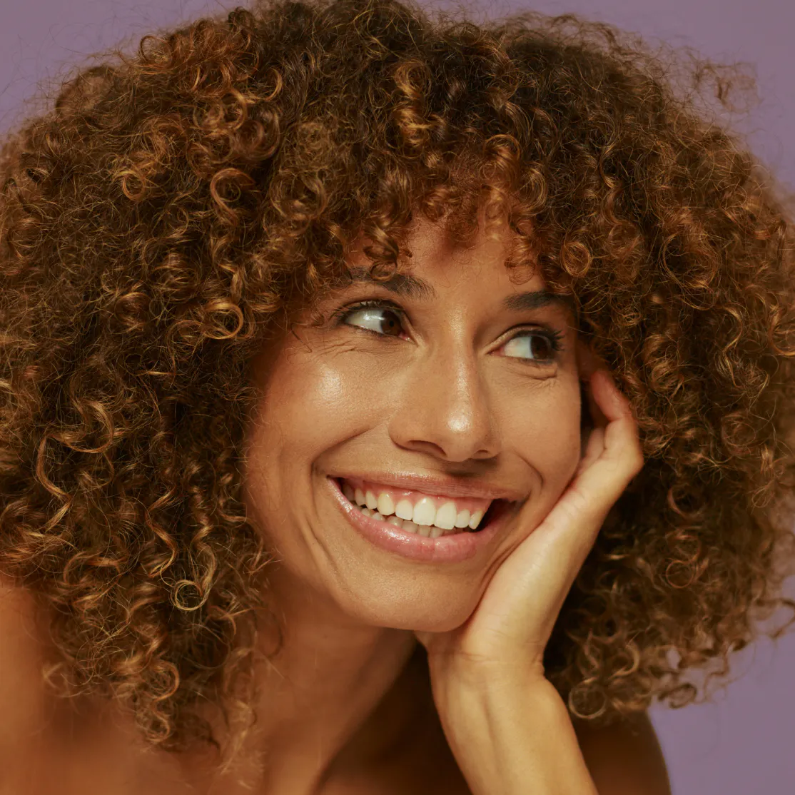 A woman in midlife smiling, resting her face in her hand.