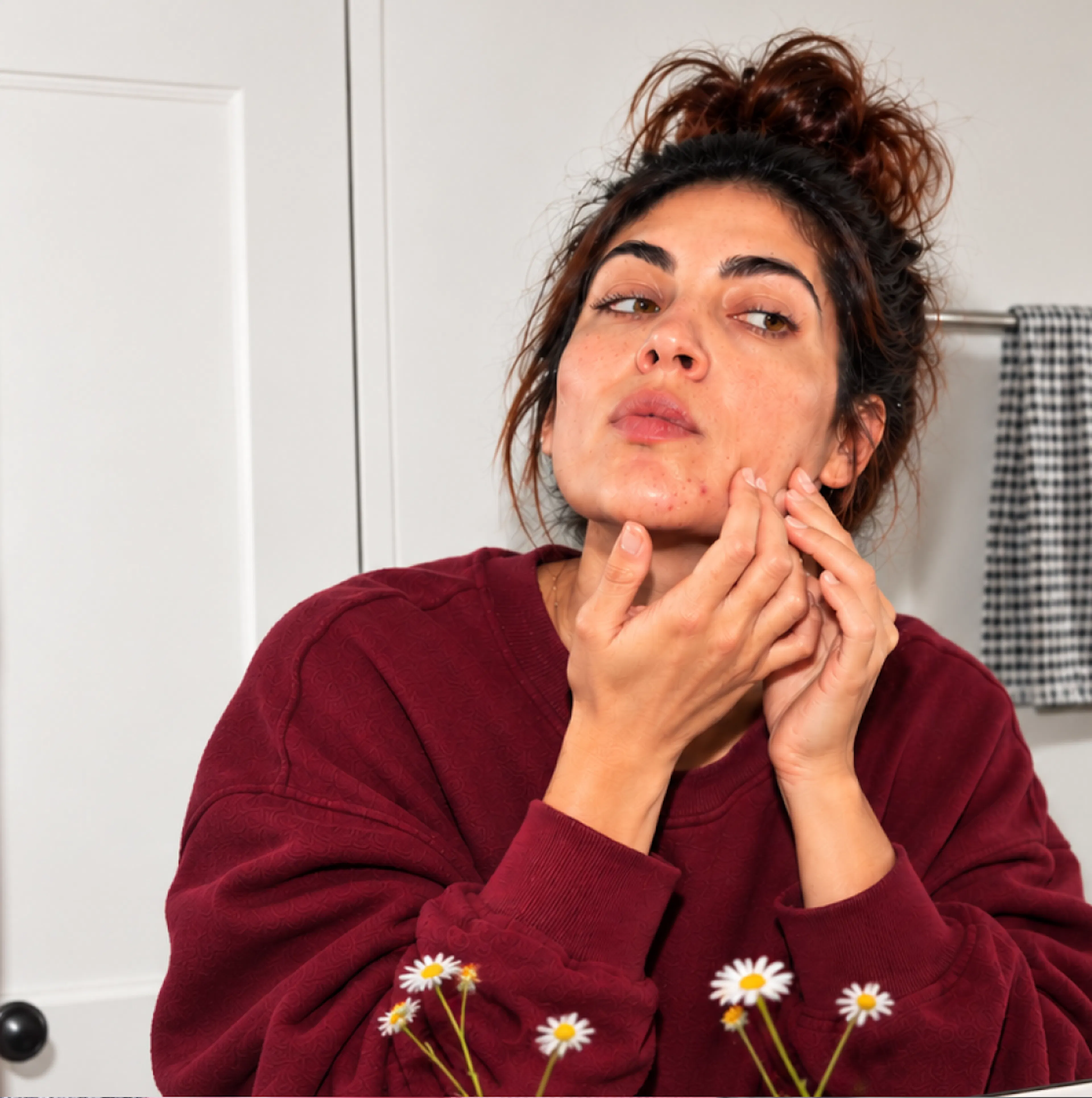 A woman in midlife, looking in the mirror and picking at her face.