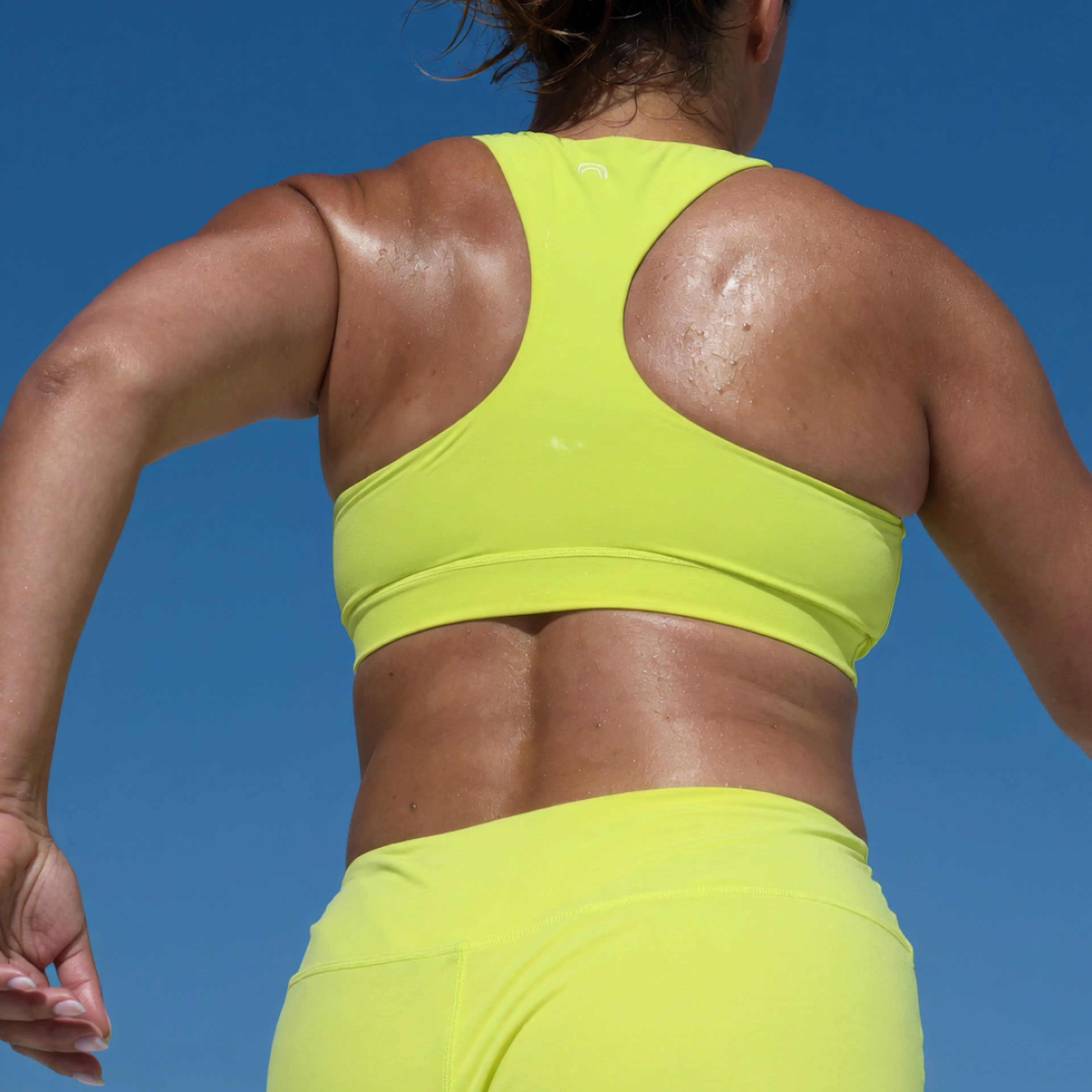 A close-up image of a woman working out outside. She's wearing a neon yellow workout set.