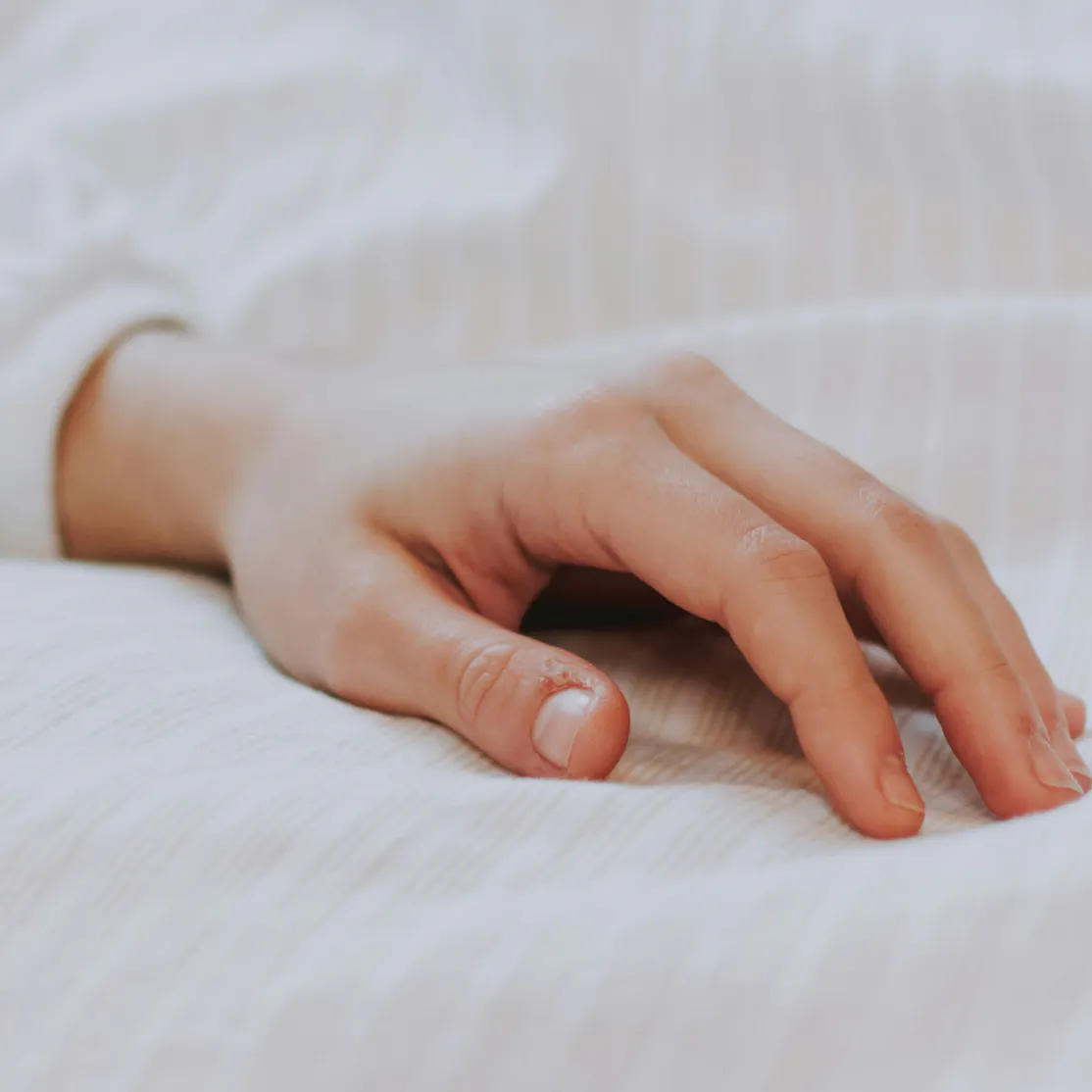 Close-up photo of a woman's hand resting on a bed.