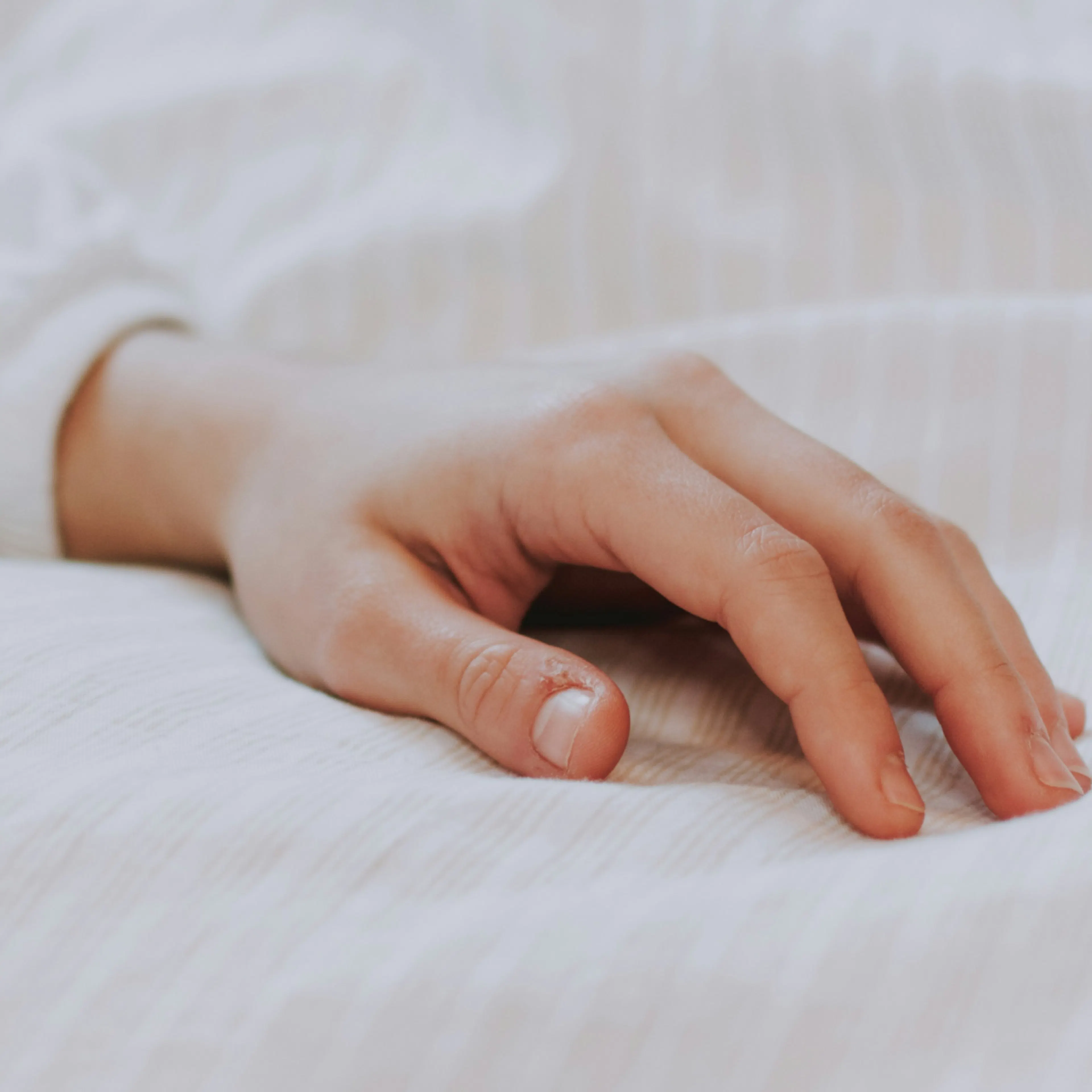 Close-up photo of a woman's hand resting on a bed.