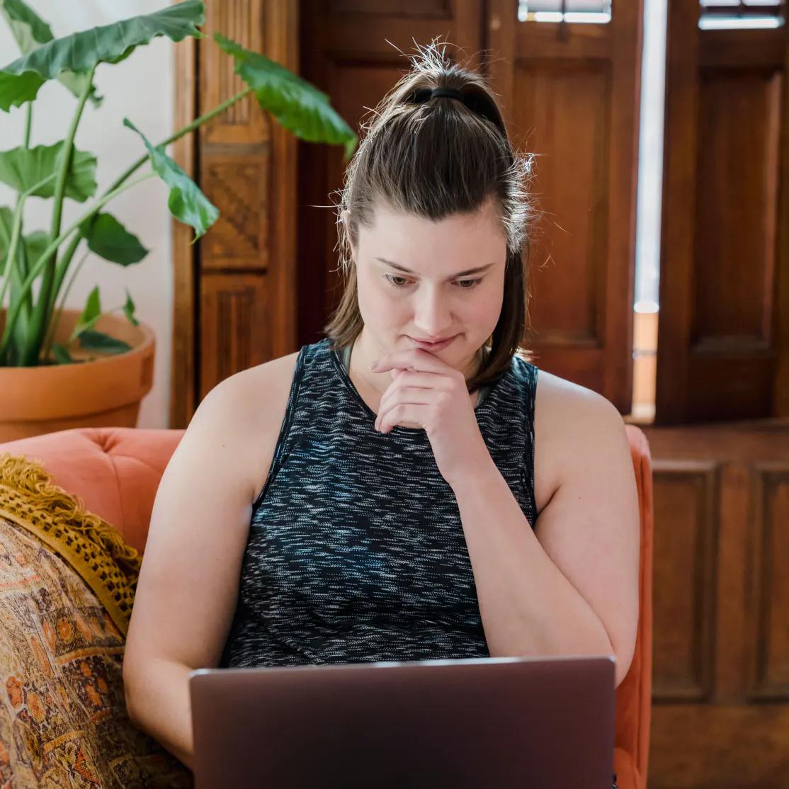 A woman looking at her laptop and thinking.