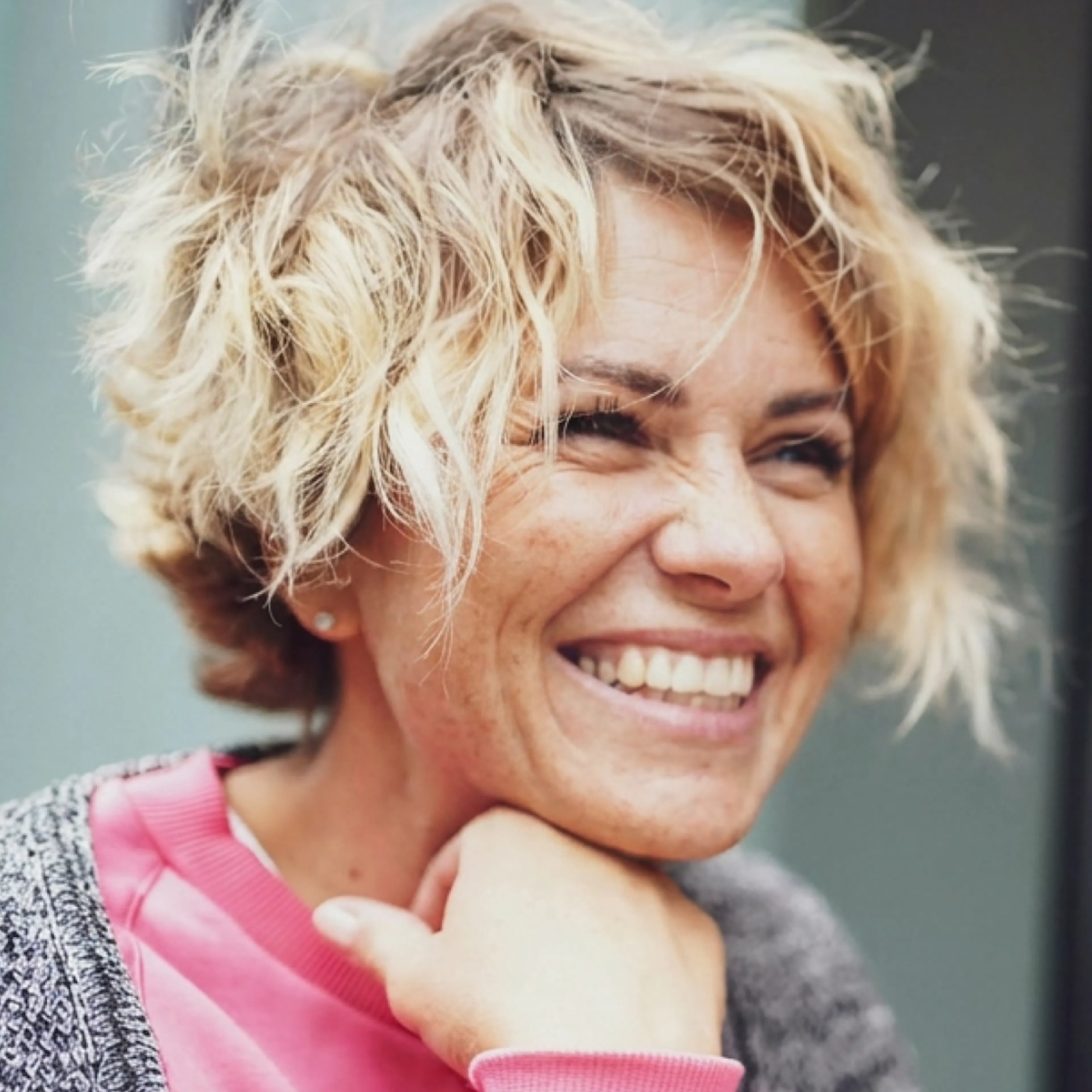 A woman in midlife with short blonde hair, smiling and looking into the distance.