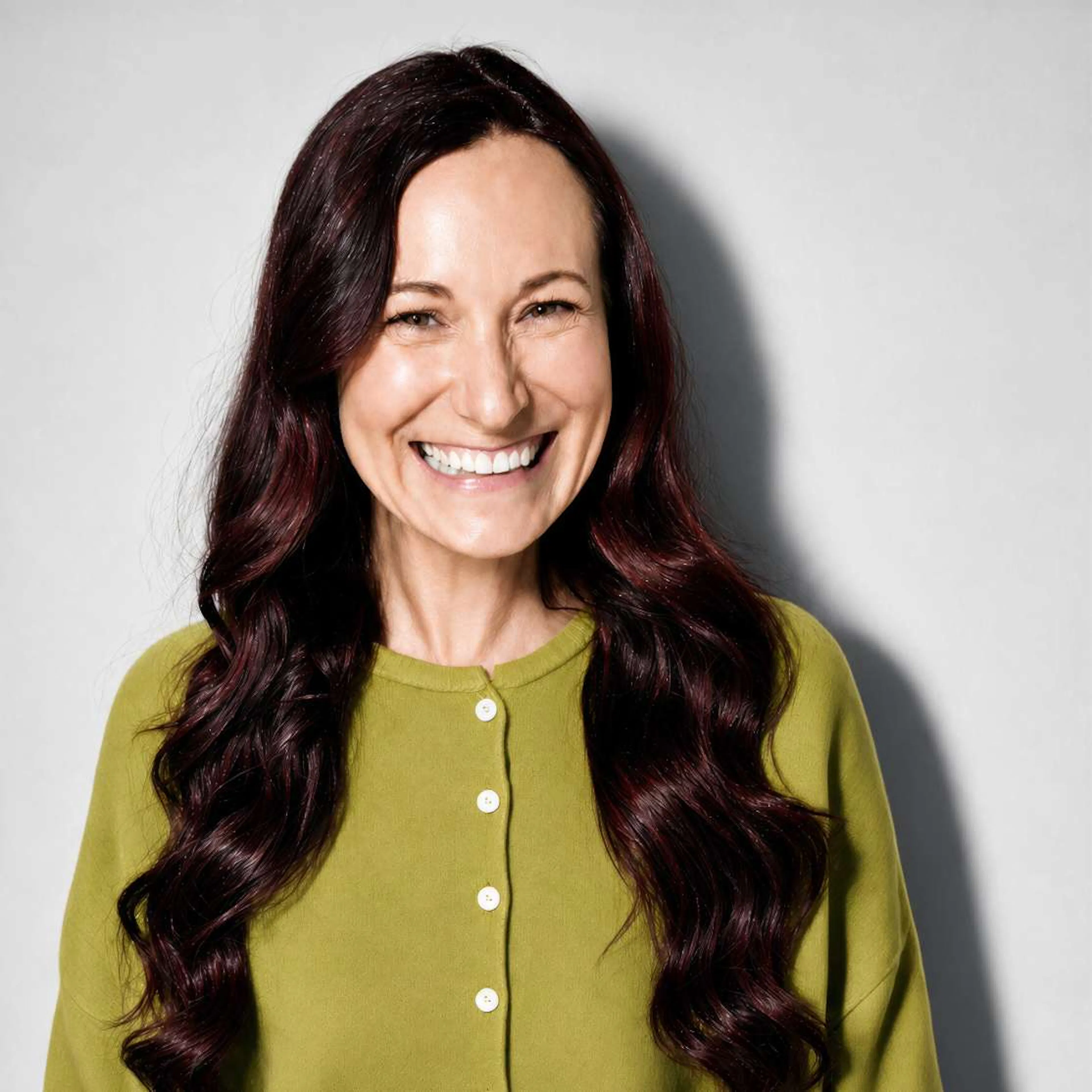 A smiling woman in midlife, wearing a green cardigan.