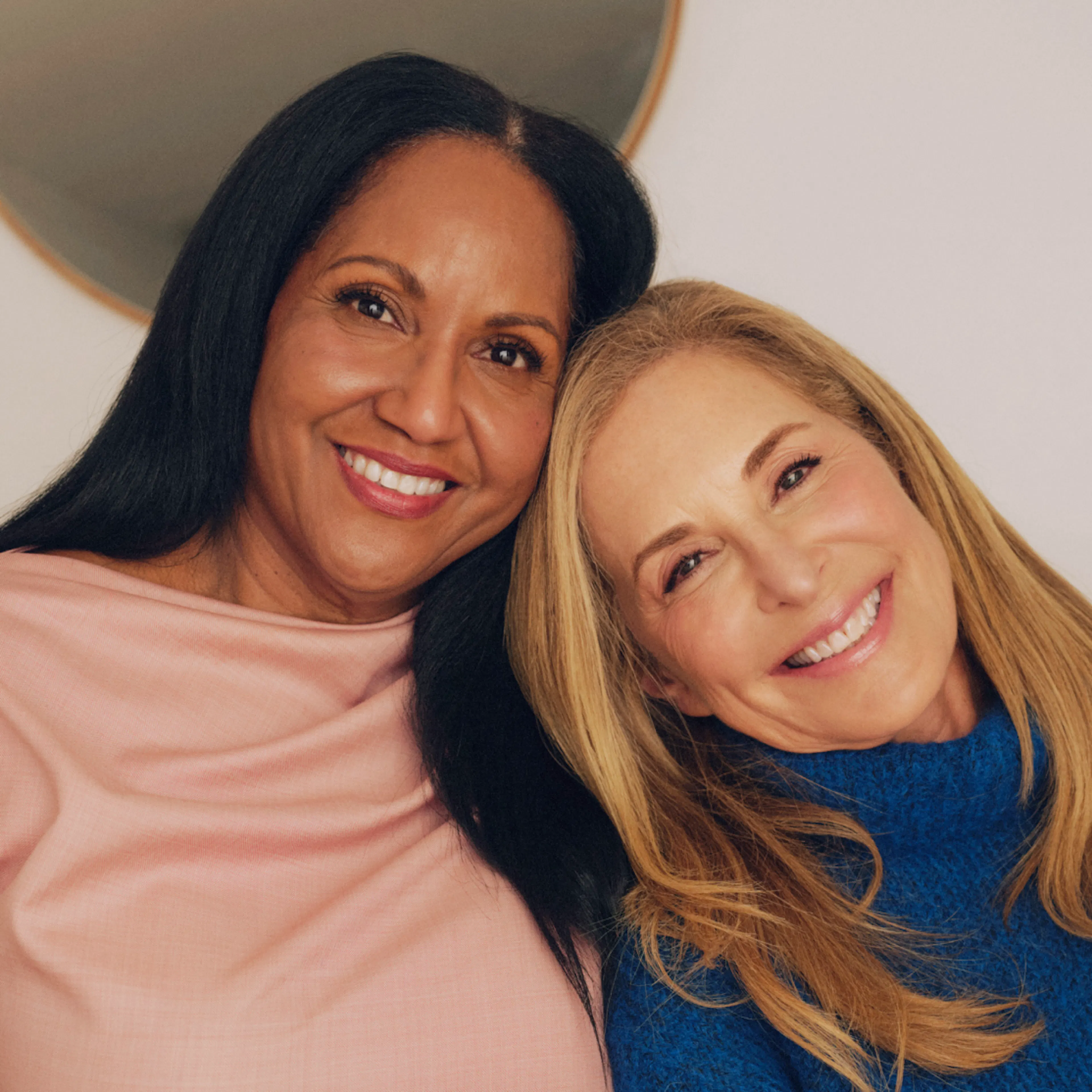 Two women in menopause smiling and leaning towards one another.