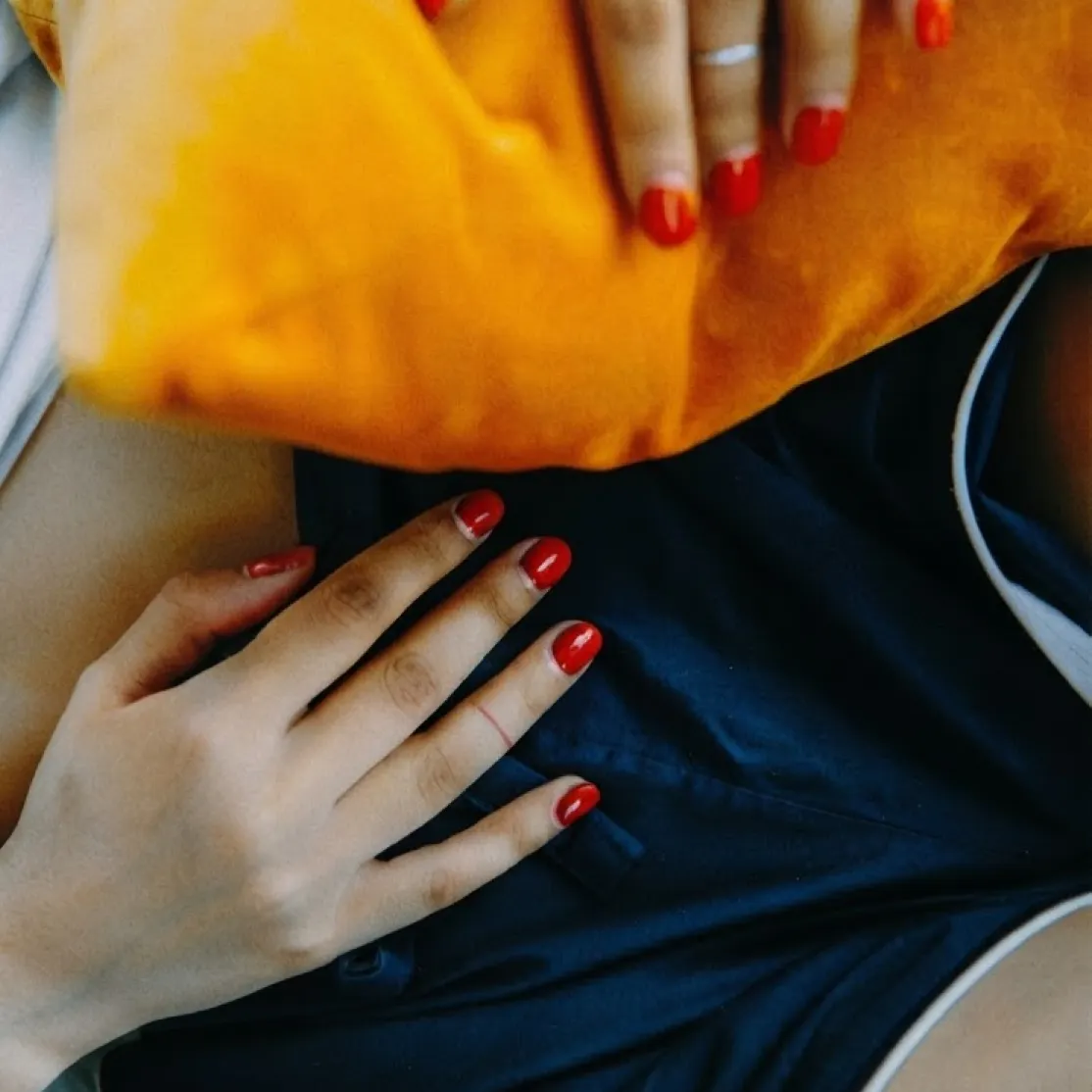 A close-up photo of a woman's hands on her pelvis on top of her shorts. She's experiencing symptoms of endometriosis.