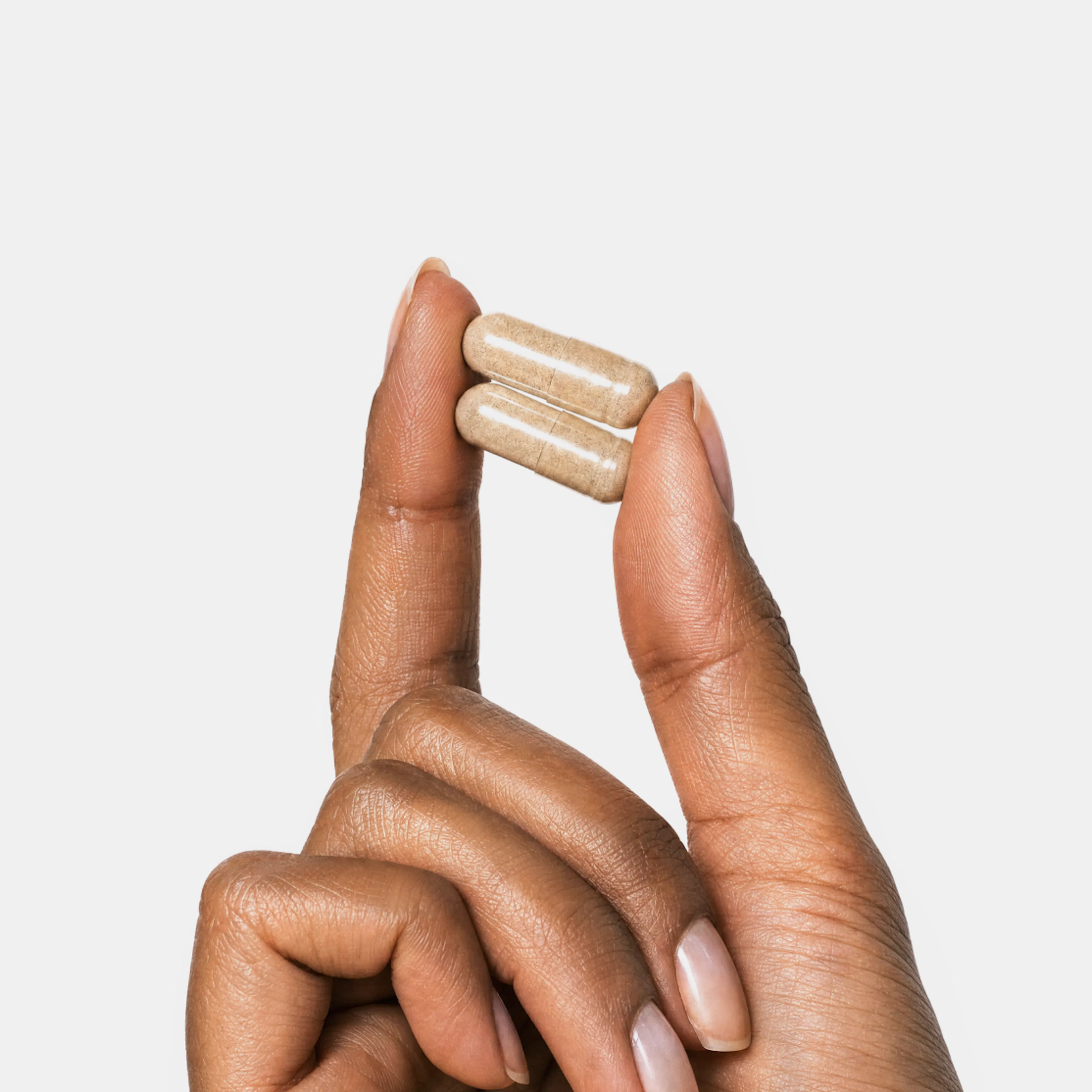 A close-up image of a woman holding two supplement capsules in her hand.