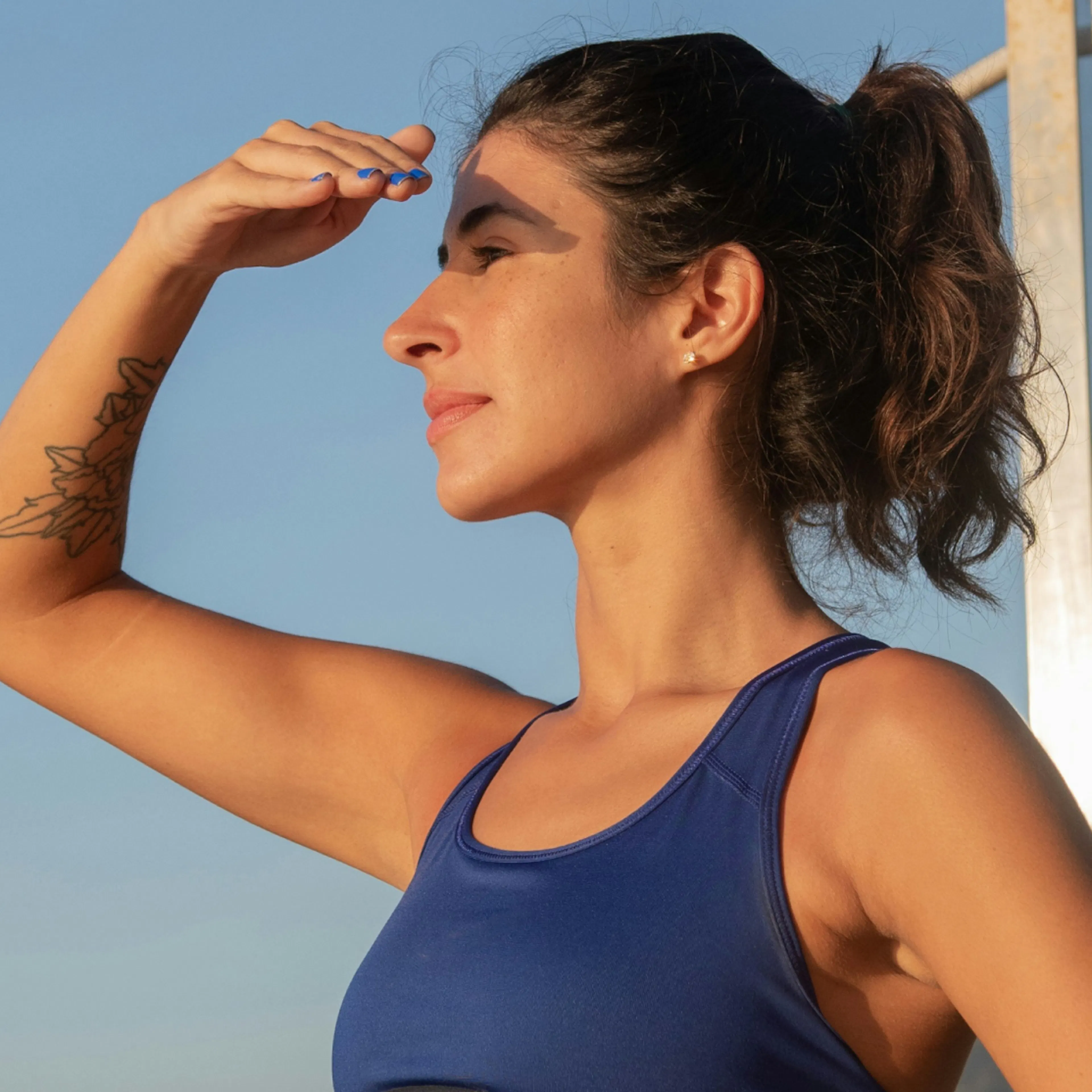 A woman in midlife exercising outside, looking into the distance at dusk. She is wearing a blue tank top.