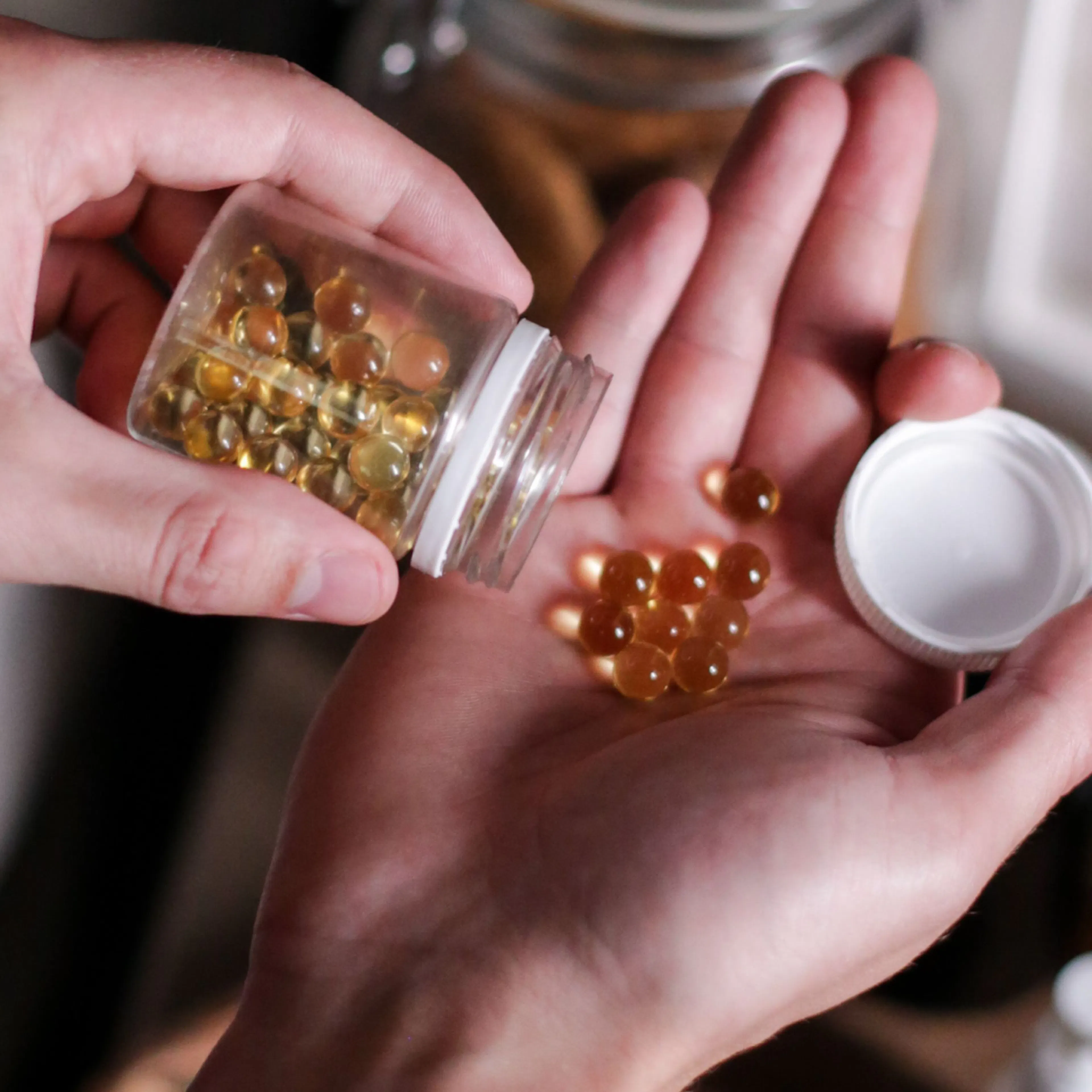 An image of a woman holding capsules in her hand after pouring them from a glass container.