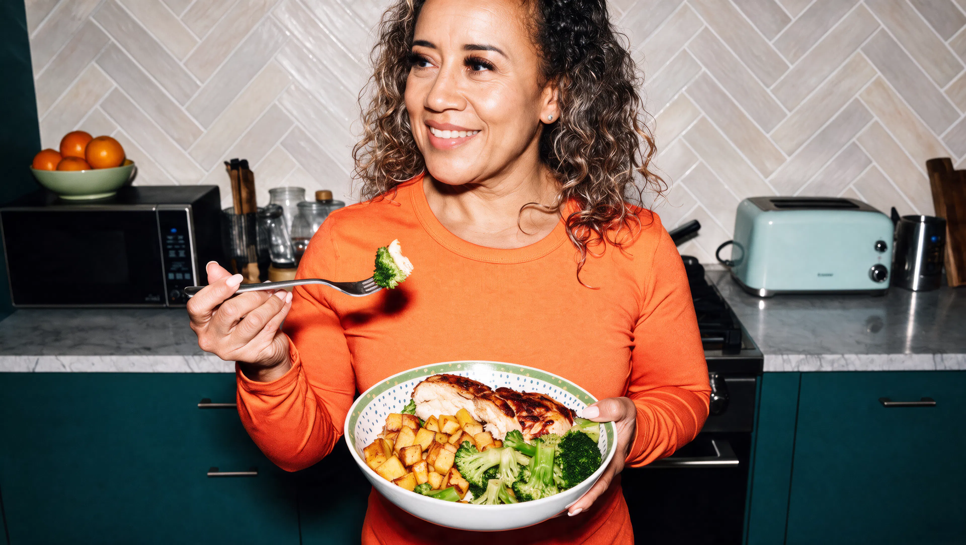 woman eating a chicken salad smiling in her kitchen