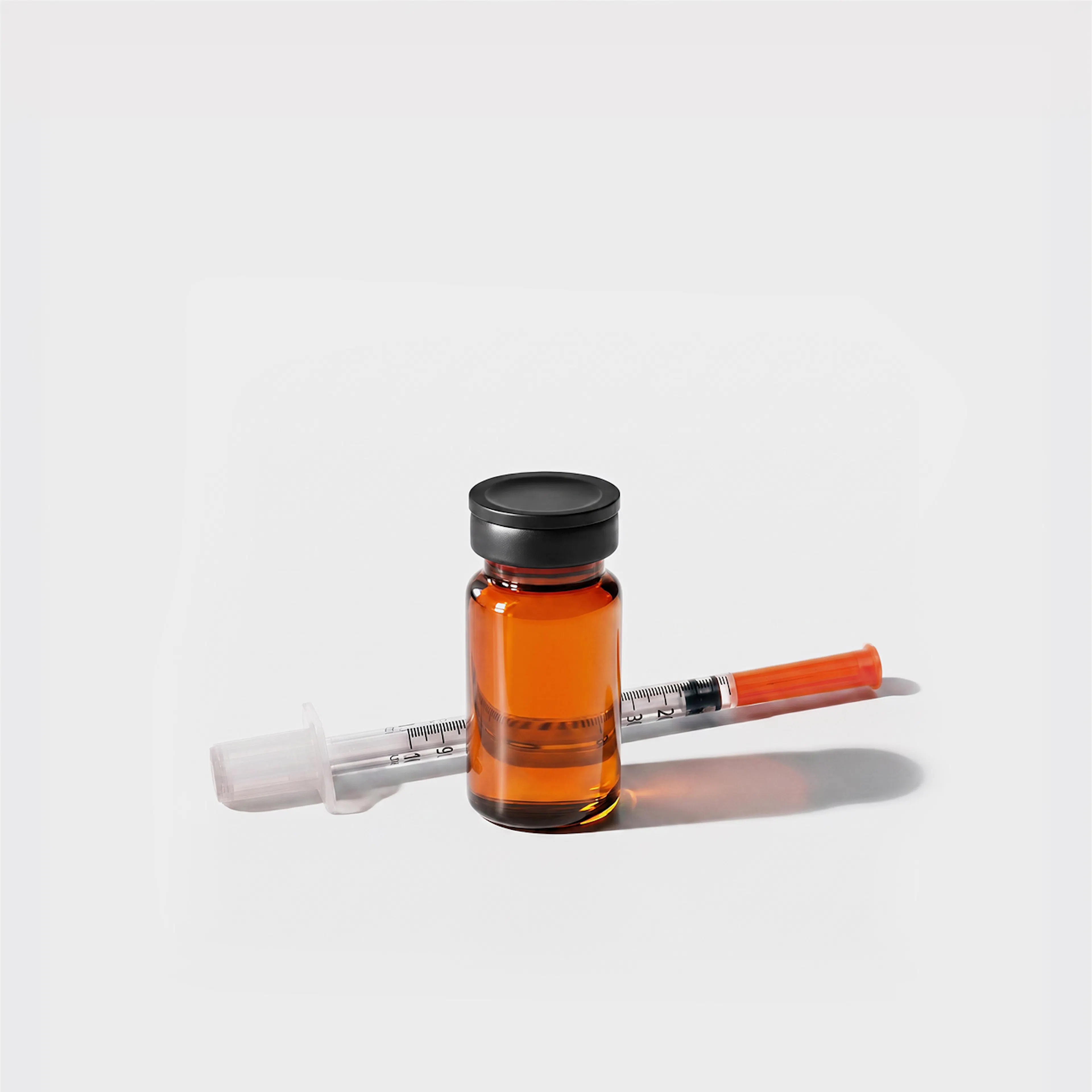 Glass vial standing beside thin syringe